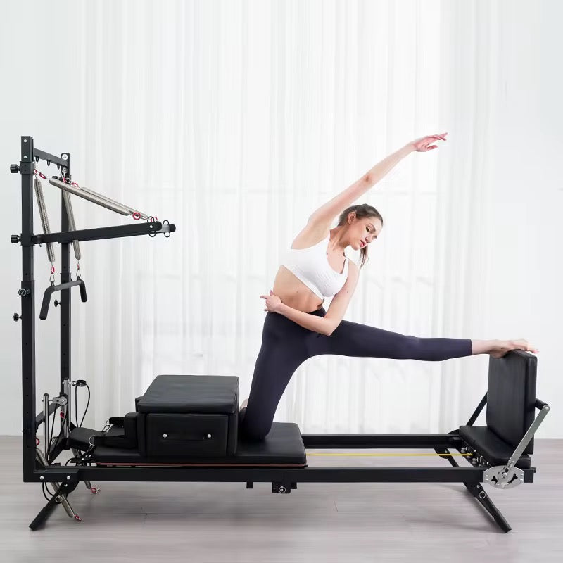 Una mujer en ropa deportiva hace estiramientos de pilates en un reformer frente a cortinas blancas.