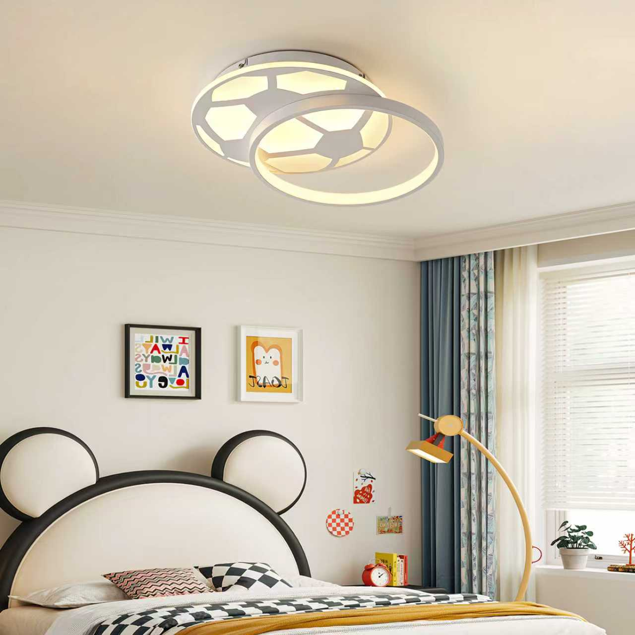 Ein Kinderzimmer mit Bärenbett, weißer Deckenleuchte, farbigen Bildern, Standlampe und Vorhängen am Fenster.