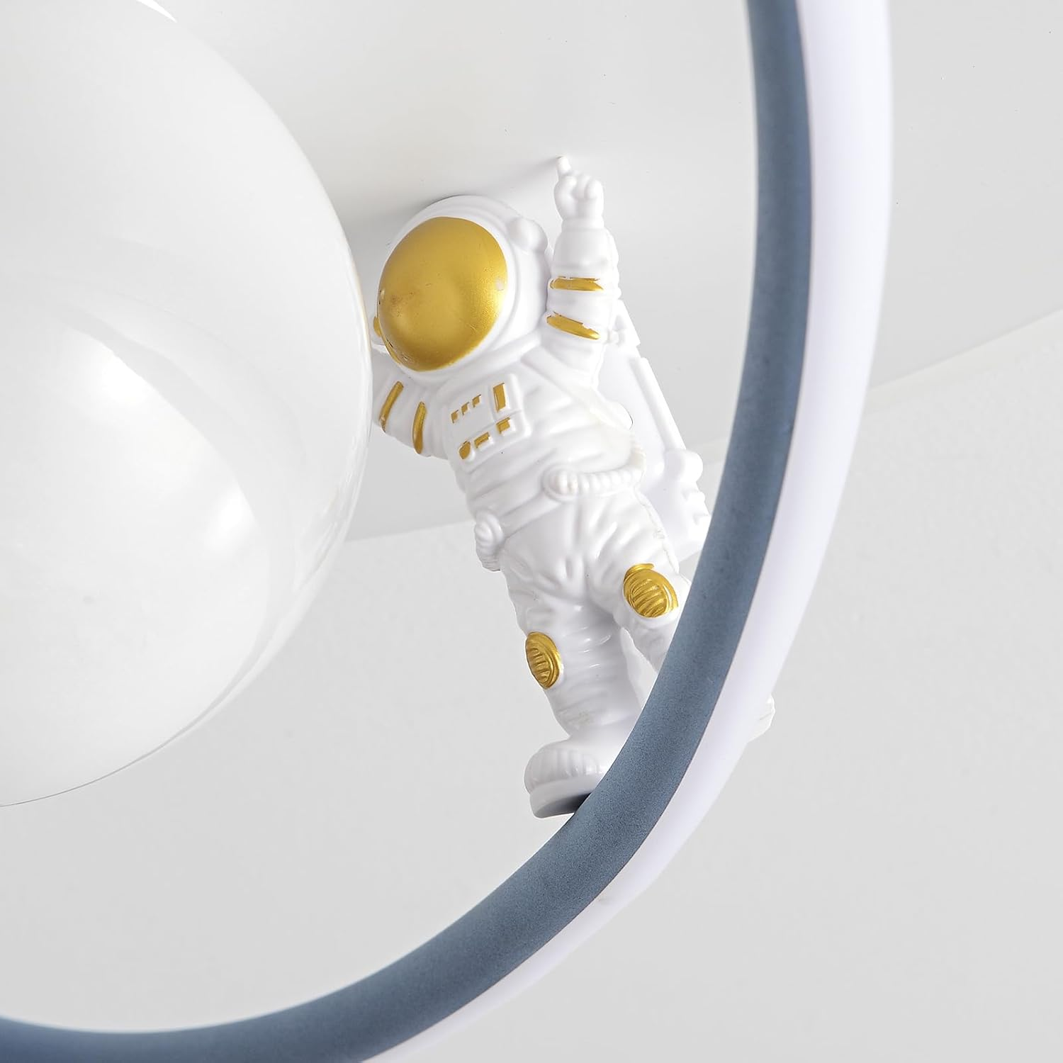 Eine weiße Astronautenfigur mit goldenen Details klettert vor weißem Hintergrund auf eine moderne ringförmige Leuchte.
