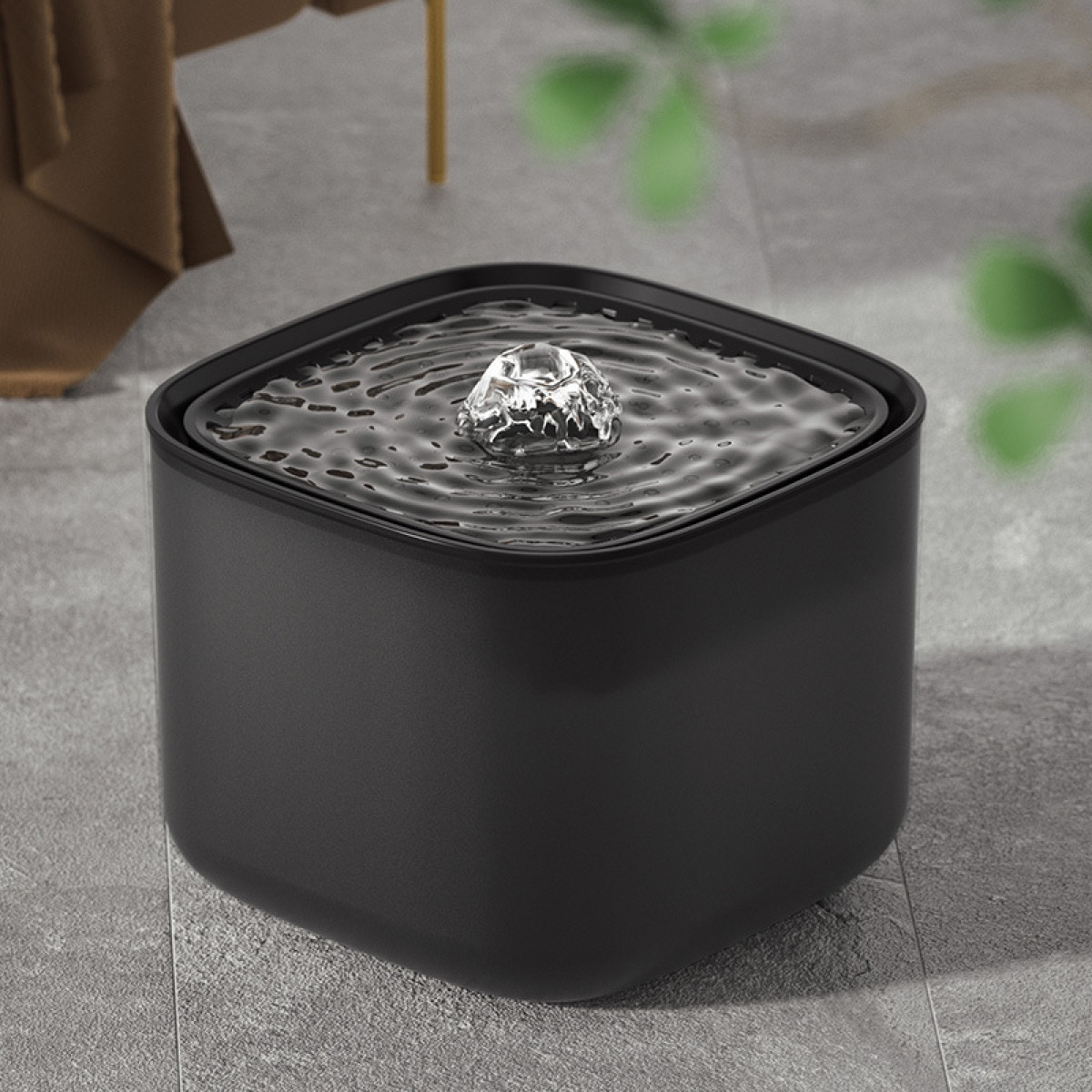 Ein schwarzer, quadratischer Wasserspender mit sprudelndem Wasser auf einem grauen Fliesenboden.
