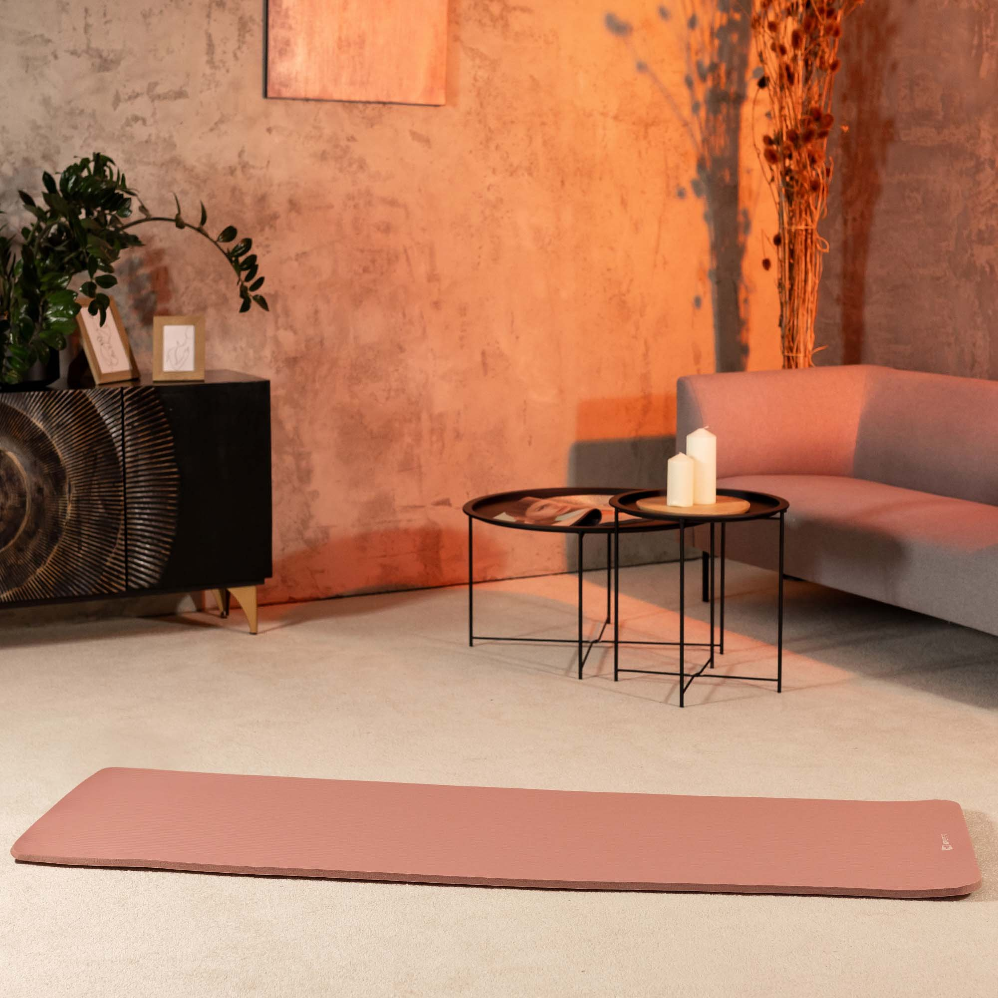 Eine rosa Yogamatte liegt auf dem Teppich in einem warm erleuchteten Zimmer mit Sofa und Beistelltischen.