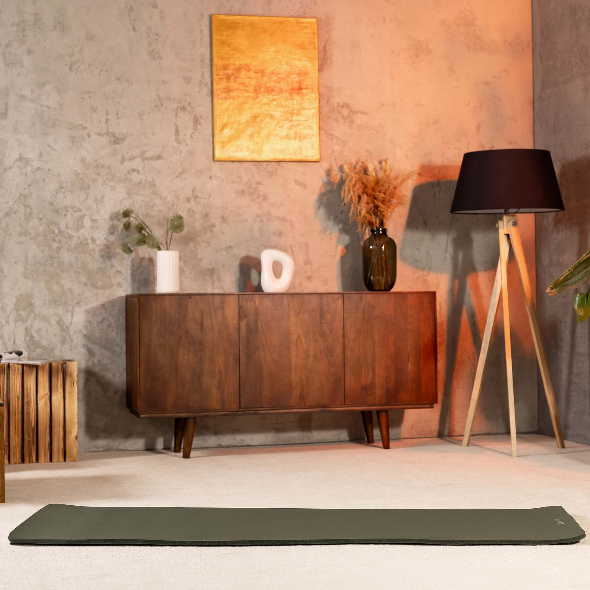 Eine grüne Yoga-Matte liegt auf dem Teppich in einem modernen Zimmer mit Holzkommode und Lampe.