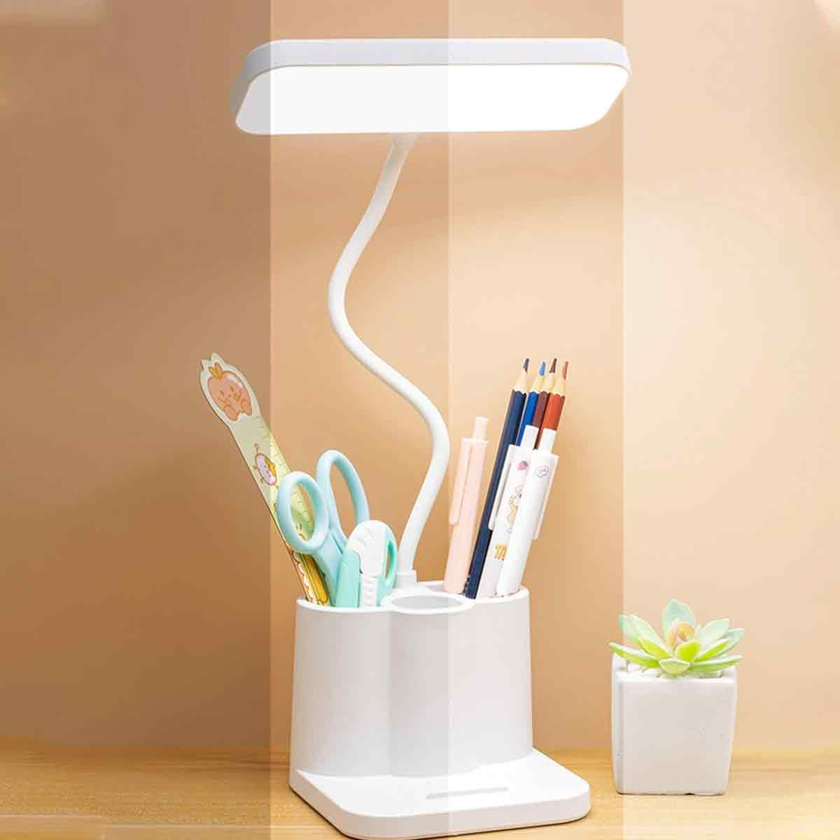 Eine weiße Schreibtischlampe mit flexiblem Hals und Stiftehalter mit Stiften und Schere, neben einer kleinen Topfpflanze.