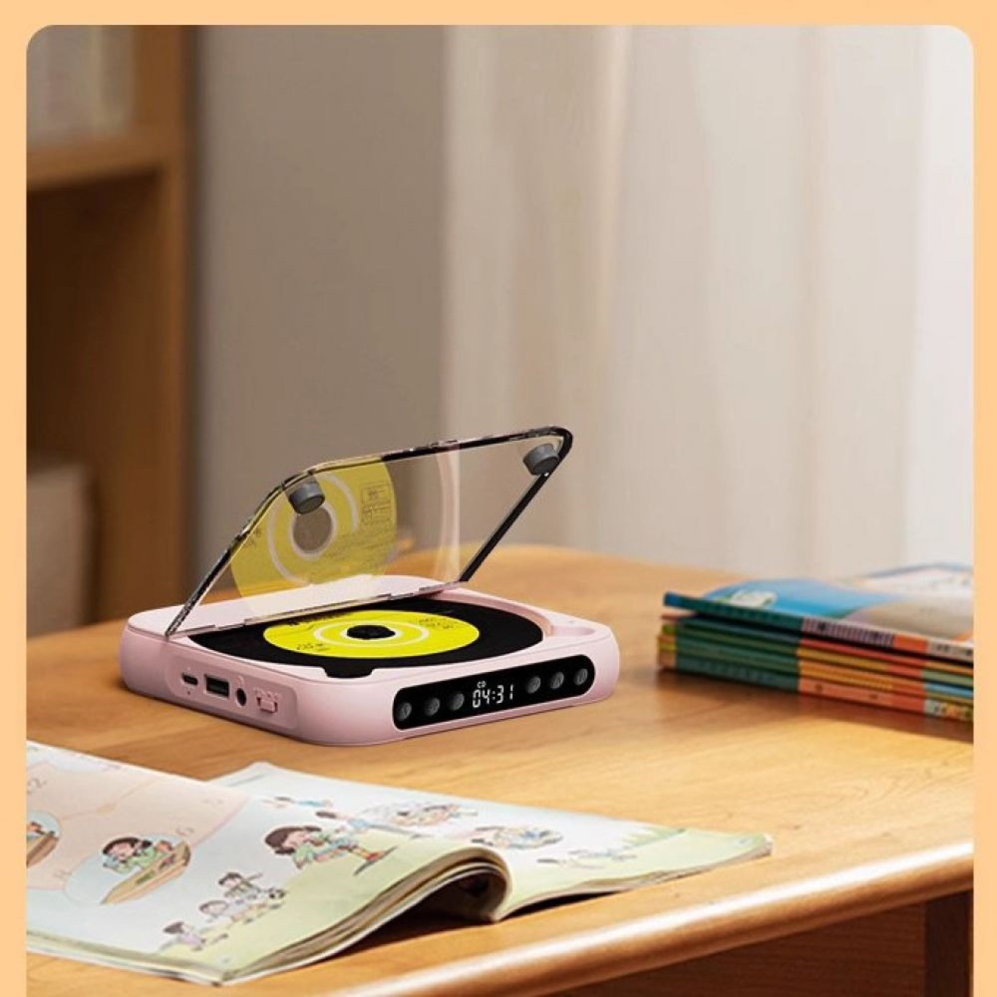 Ein rosafarbener CD-Player mit offener Abdeckung steht auf einem Holztisch, daneben liegen ein offenes Buch und ein Stapel Bücher.