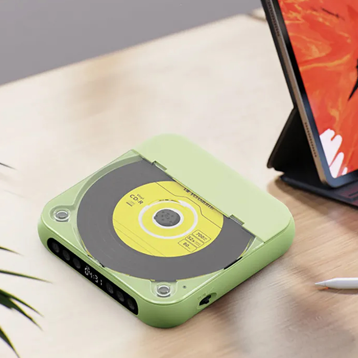 Ein grüner CD-Player mit einer CD im Inneren steht auf einem Holztisch neben einem Tablet.