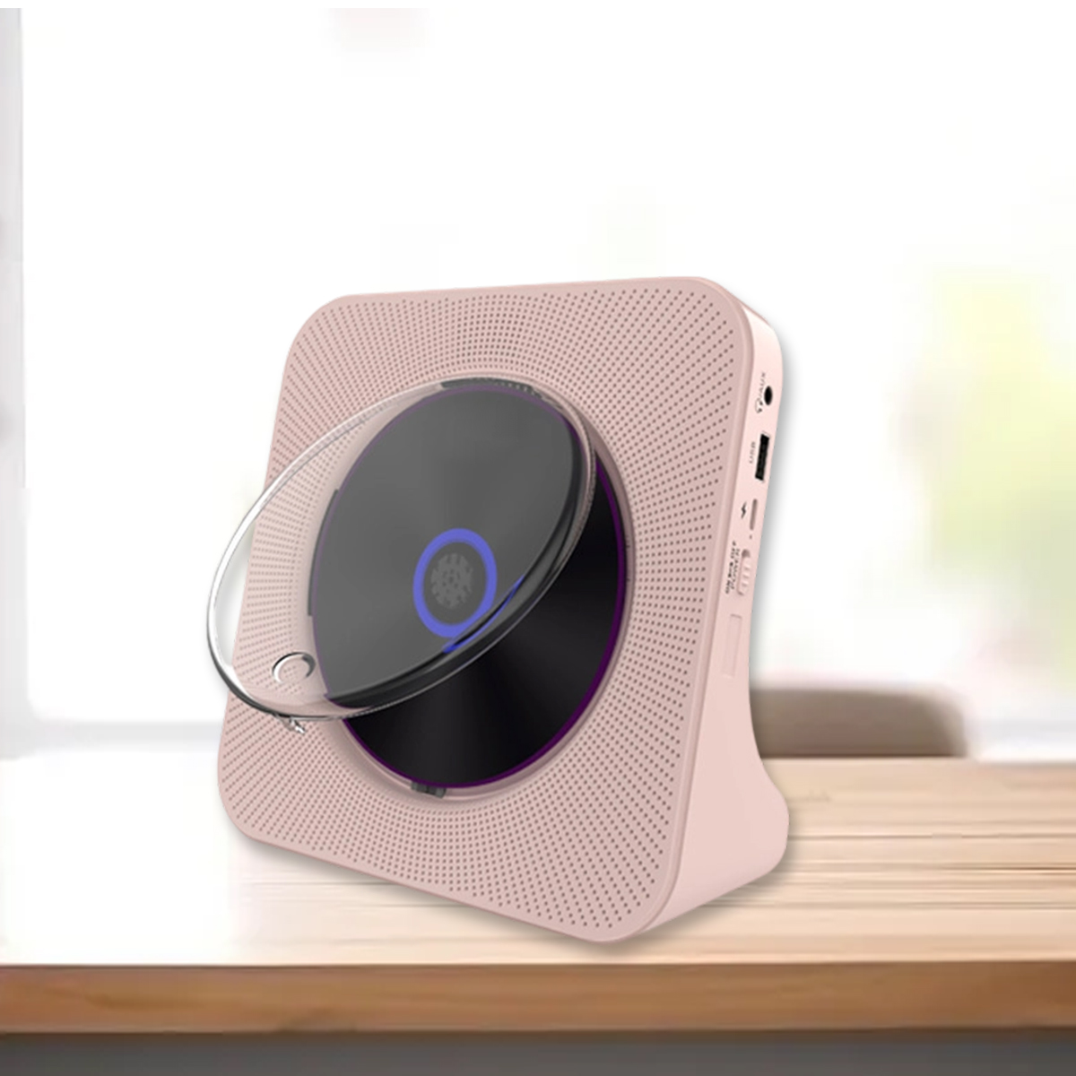 Ein rosa CD-Player mit transparenter Abdeckung steht auf einem Holztisch vor einem hellen Fenster.