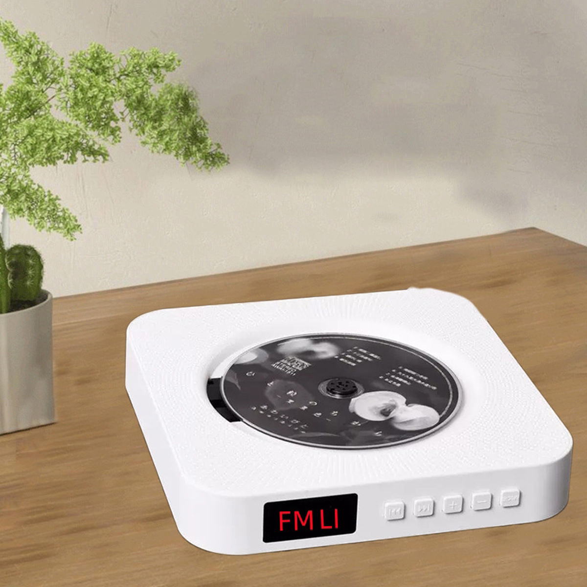 Ein weißer tragbarer CD-Player mit Digitalanzeige und Tasten steht auf einem Holztisch neben einer grünen Pflanze.