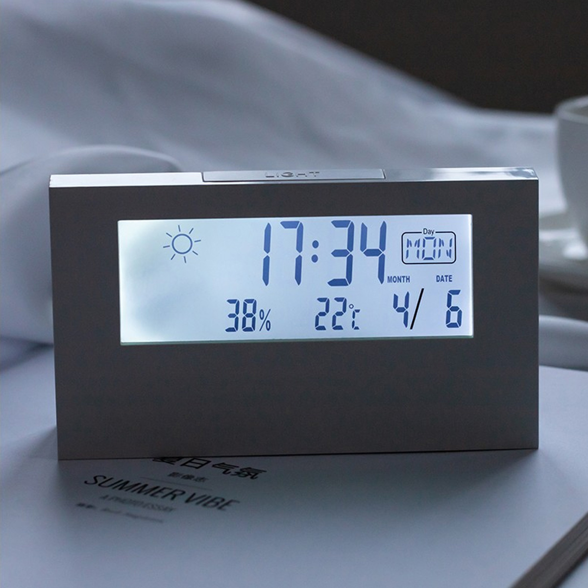 Silberner Digitalwecker mit blauem Display, der Uhrzeit, Feuchtigkeit, Temperatur und Datum anzeigt.