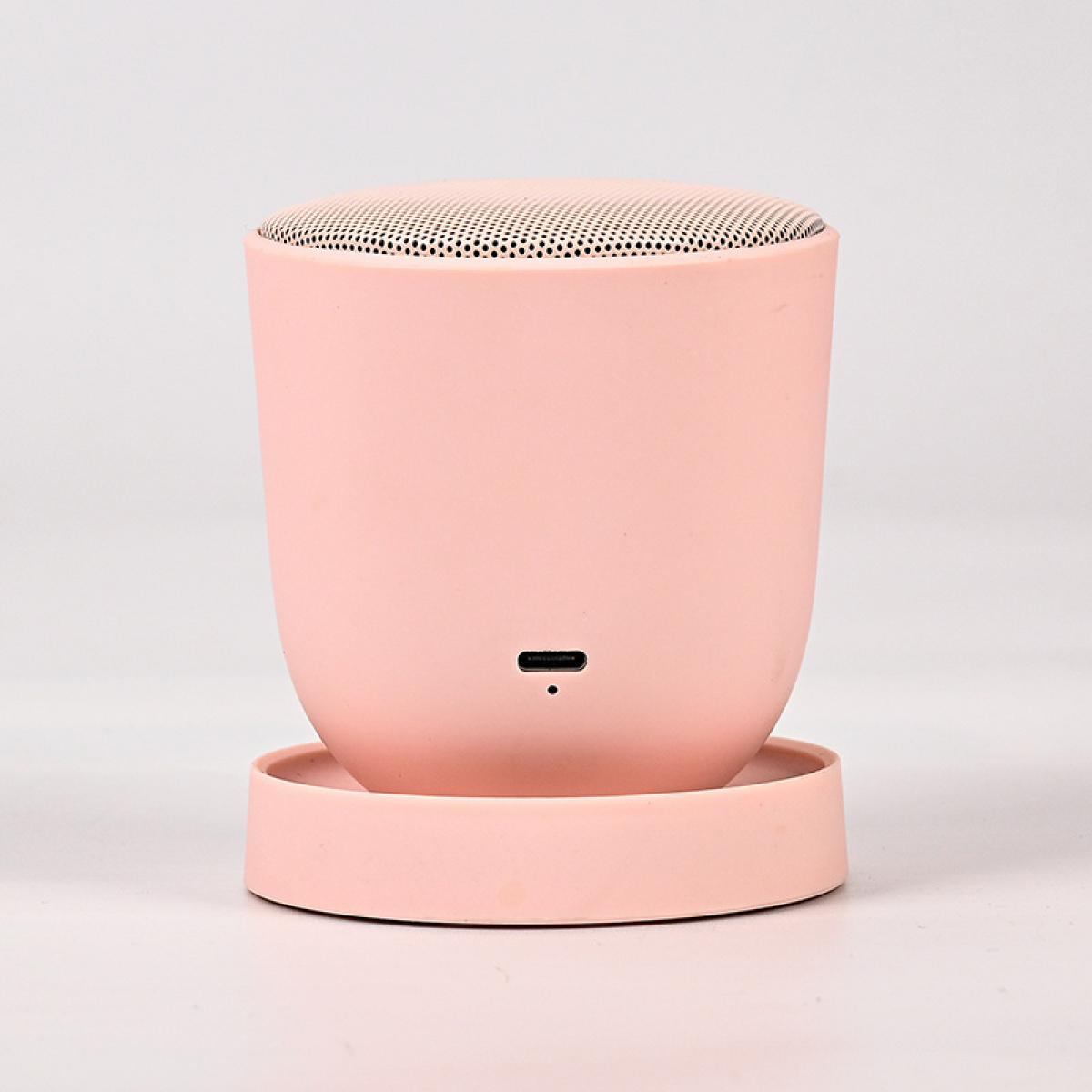 Ein pastellrosa zylindrischer Bluetooth-Lautsprecher mit Mesh-Oberseite steht auf einer passenden rosa runden Basis.