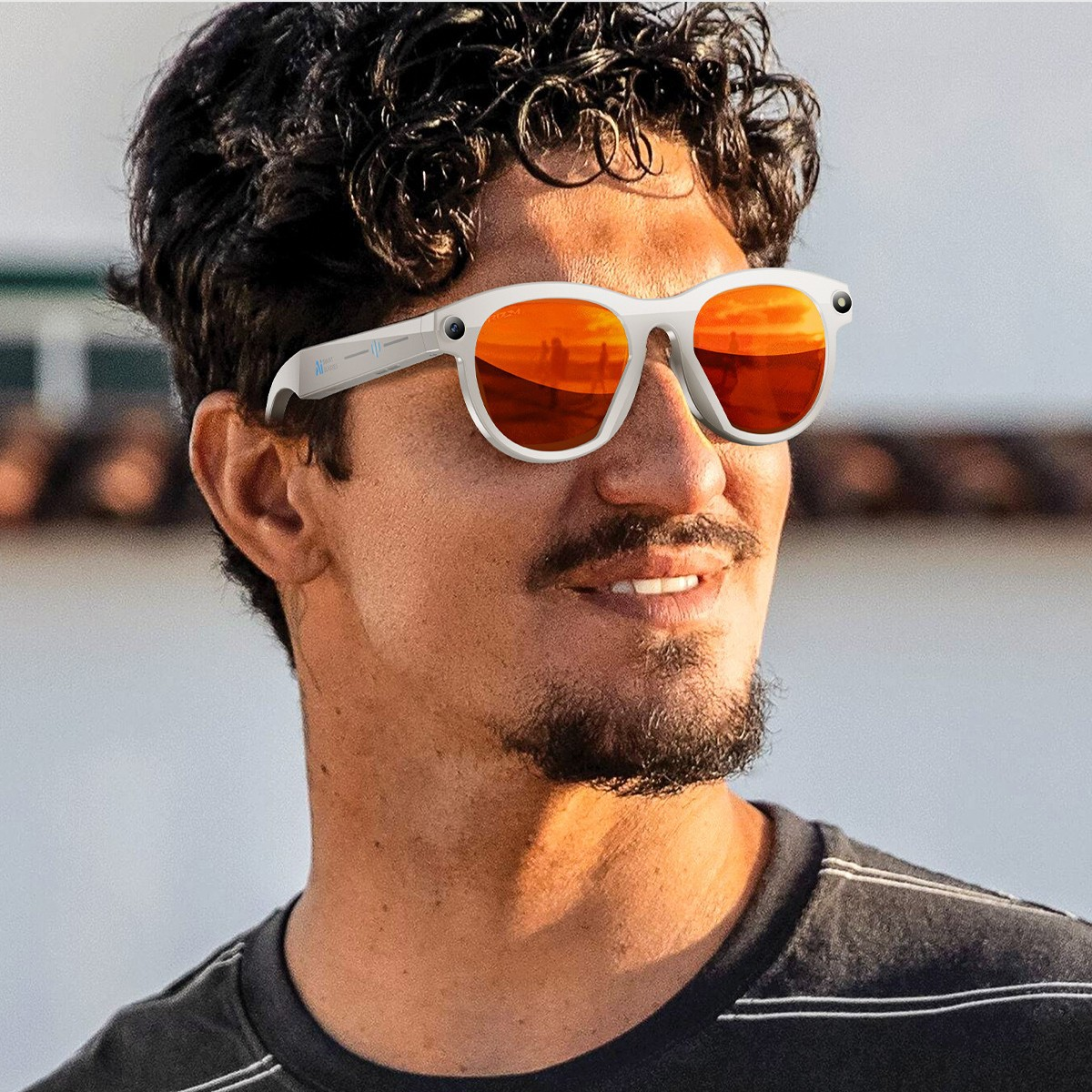 Ein Mann mit dunklem, lockigem Haar trägt weiße Sonnenbrillen mit orangefarbenen Gläsern.