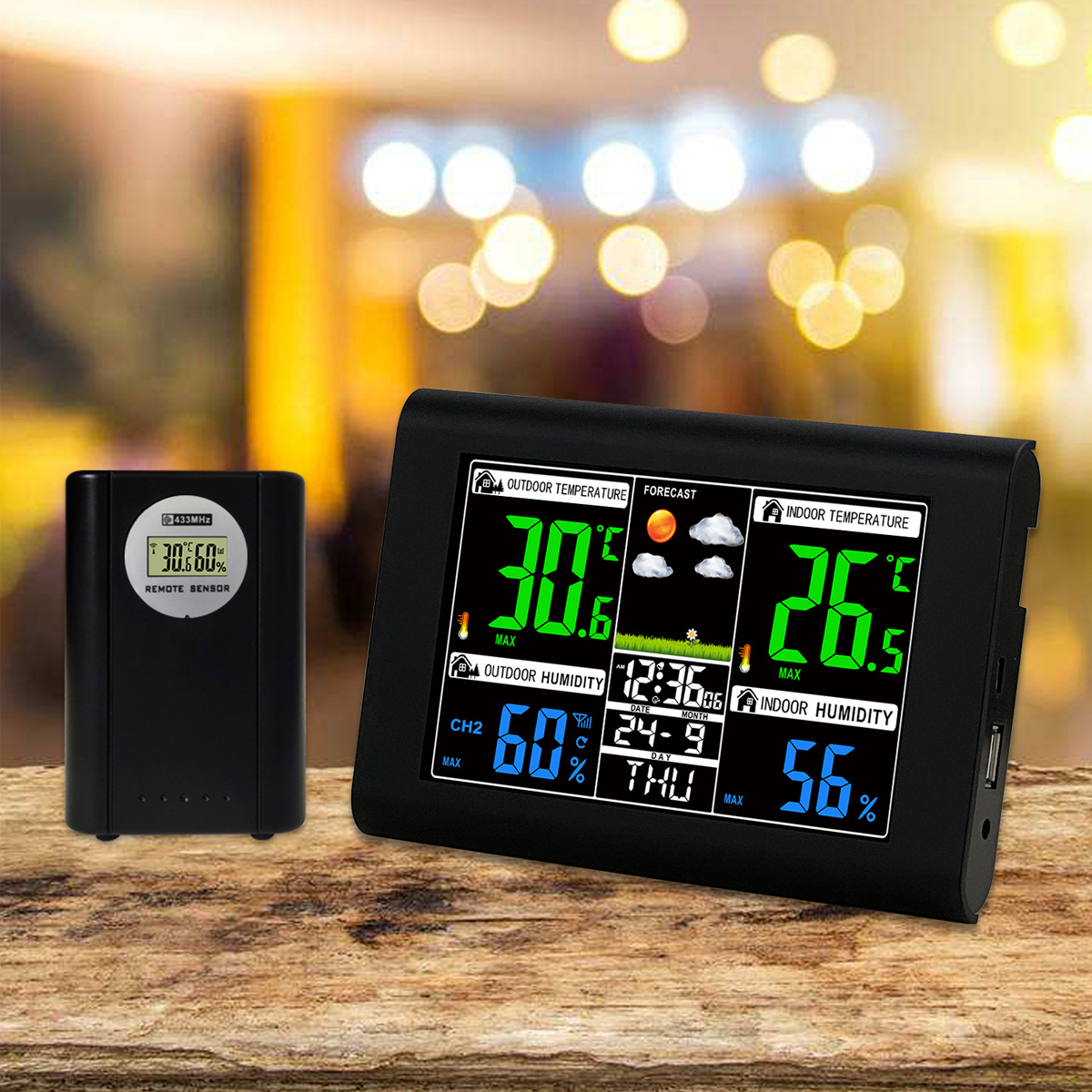 Eine schwarze Wetterstation und ein Funksensor stehen auf einem Holztisch vor einem weich gezeichneten Hintergrund.