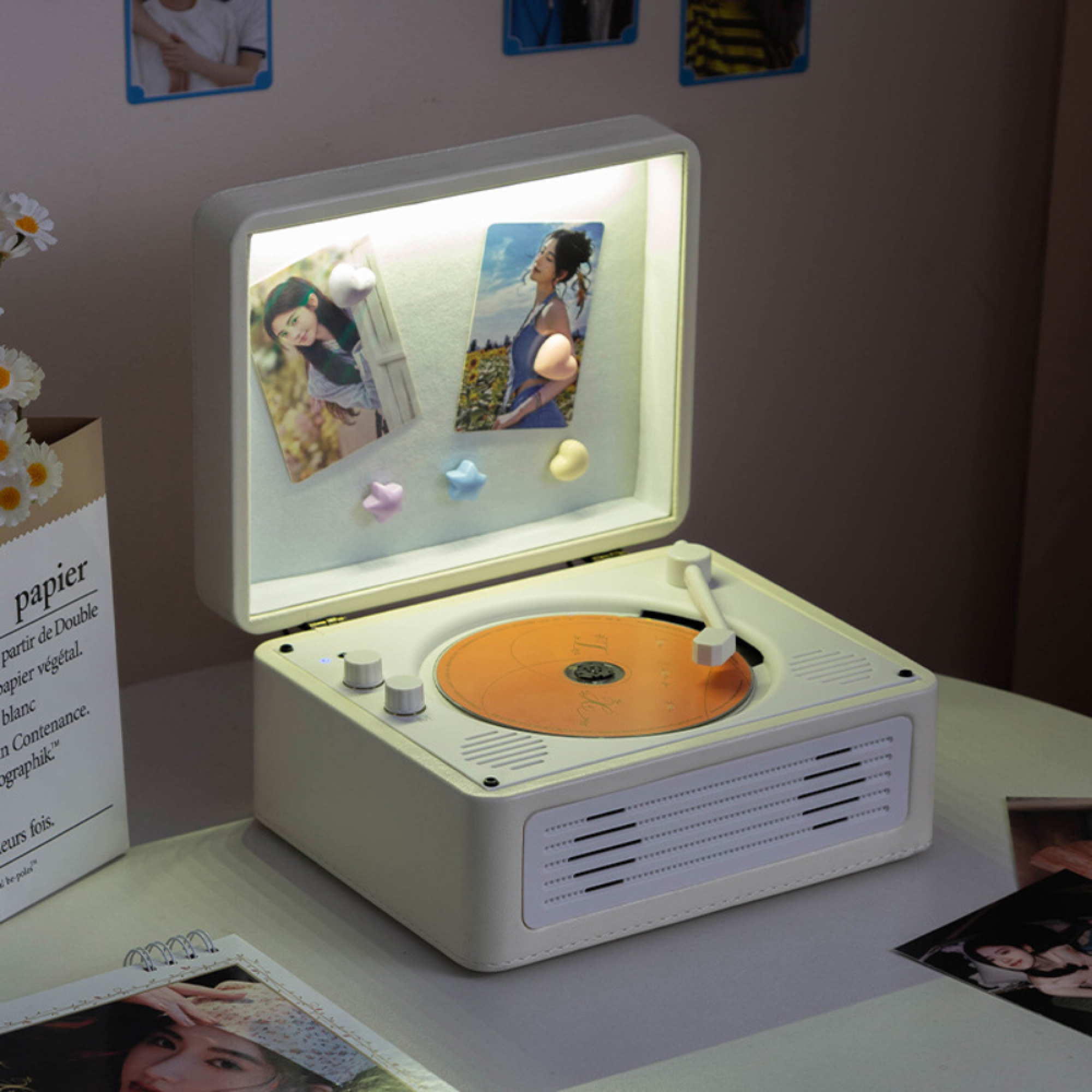 Ein cremefarbener Vintage-Plattenspieler spielt eine orange Platte, mit beleuchteten Fotokarten im offenen Deckel.