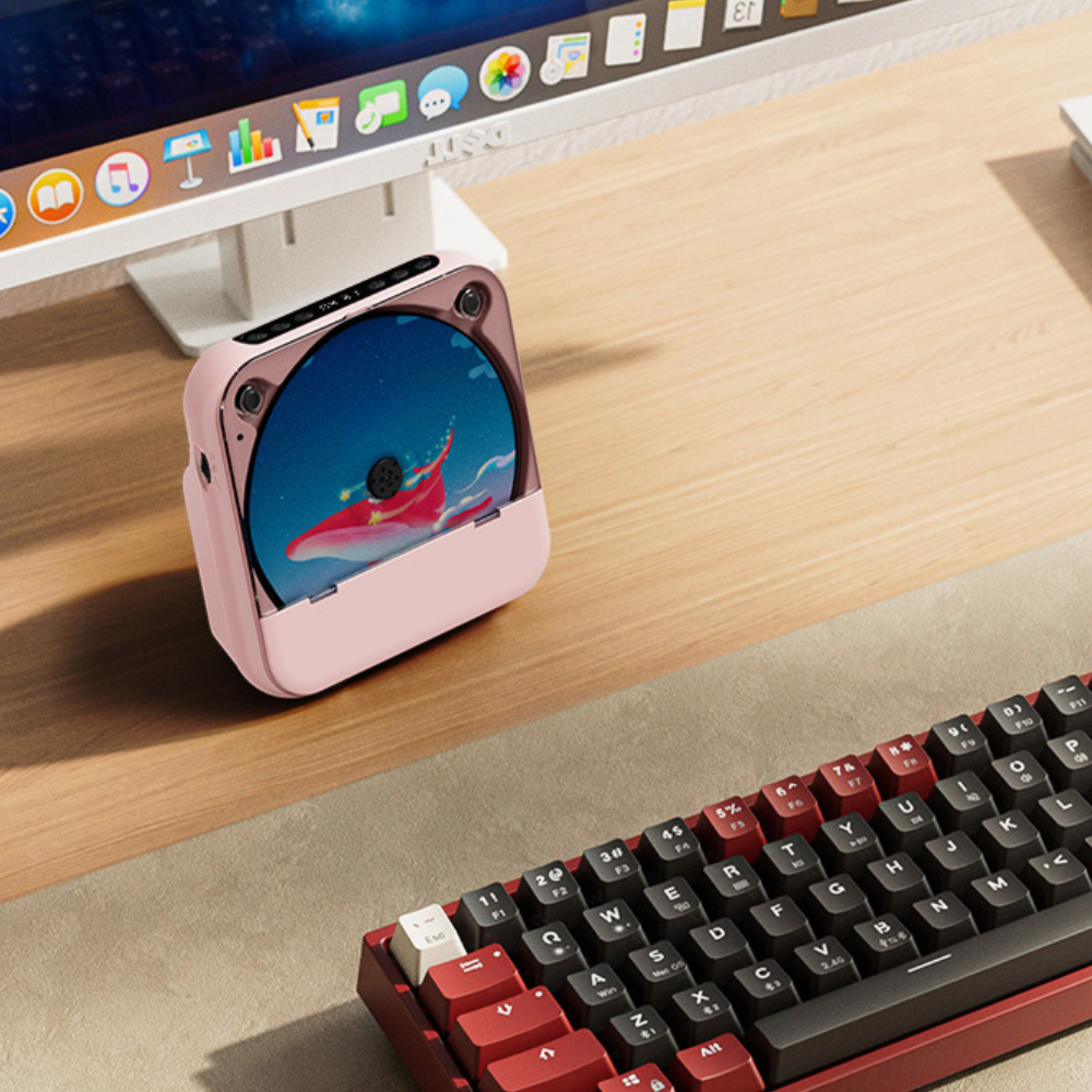 Ein rosa CD-Player steht auf einem Holztisch neben einem Computerbildschirm und einer Tastatur.
