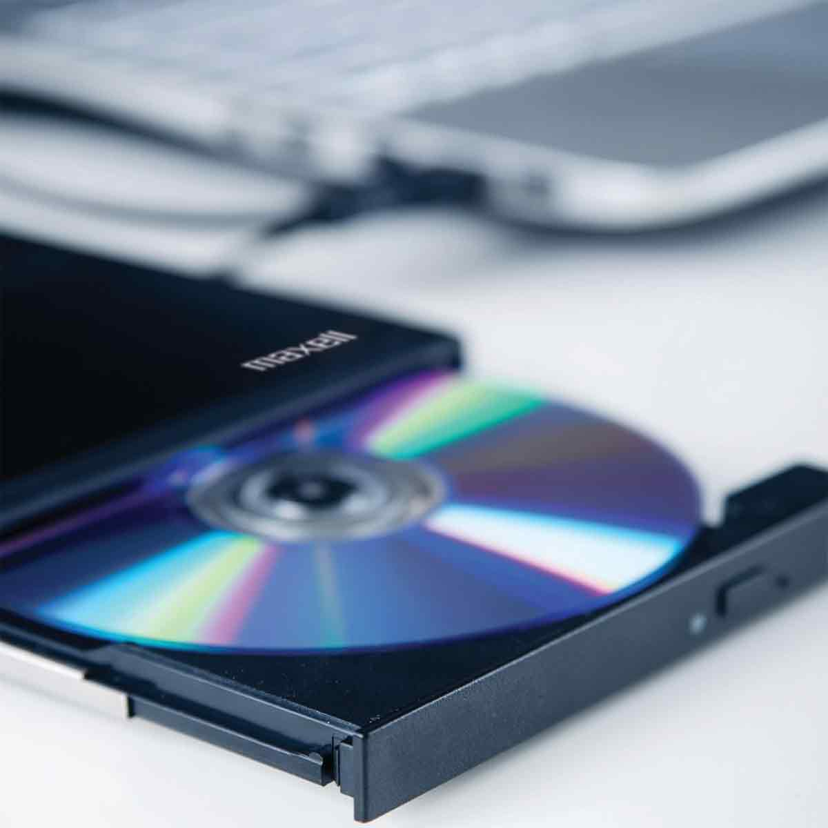 Eine bunte CD liegt im geöffneten Laufwerk eines Laptops auf weißem Grund.