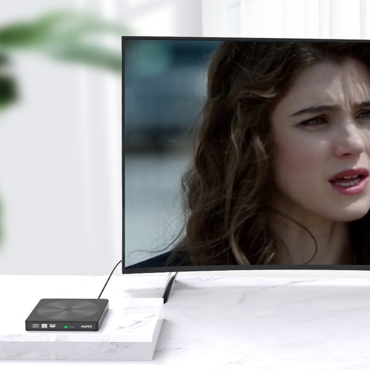 Ein schwarzes externes Laufwerk, verbunden mit einem Fernseher, der das Gesicht einer Frau zeigt, auf einem Marmortisch.