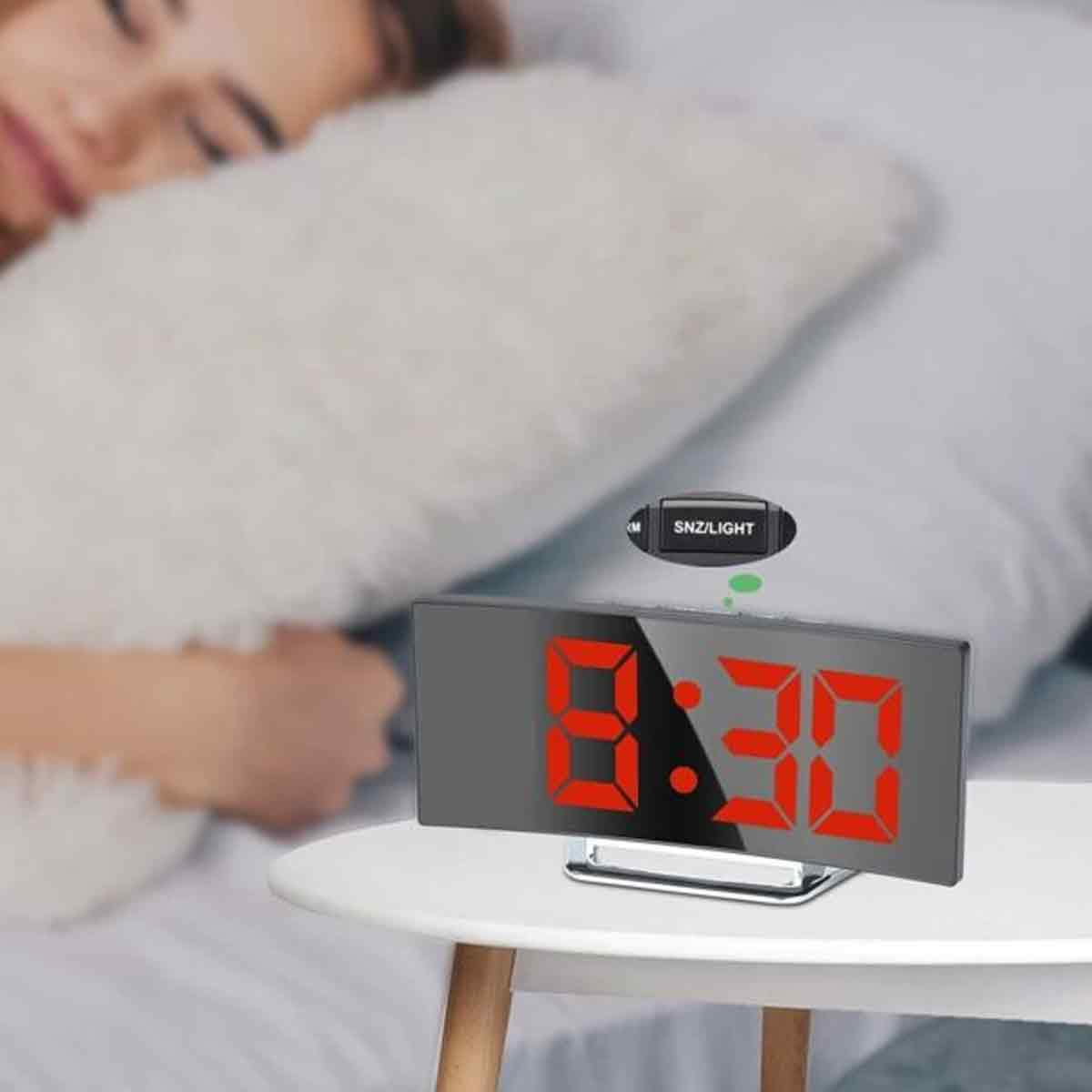 Ein digitaler Wecker mit roten Zahlen, die 8:30 anzeigen, steht auf einem weißen Nachttisch, während jemand schläft.