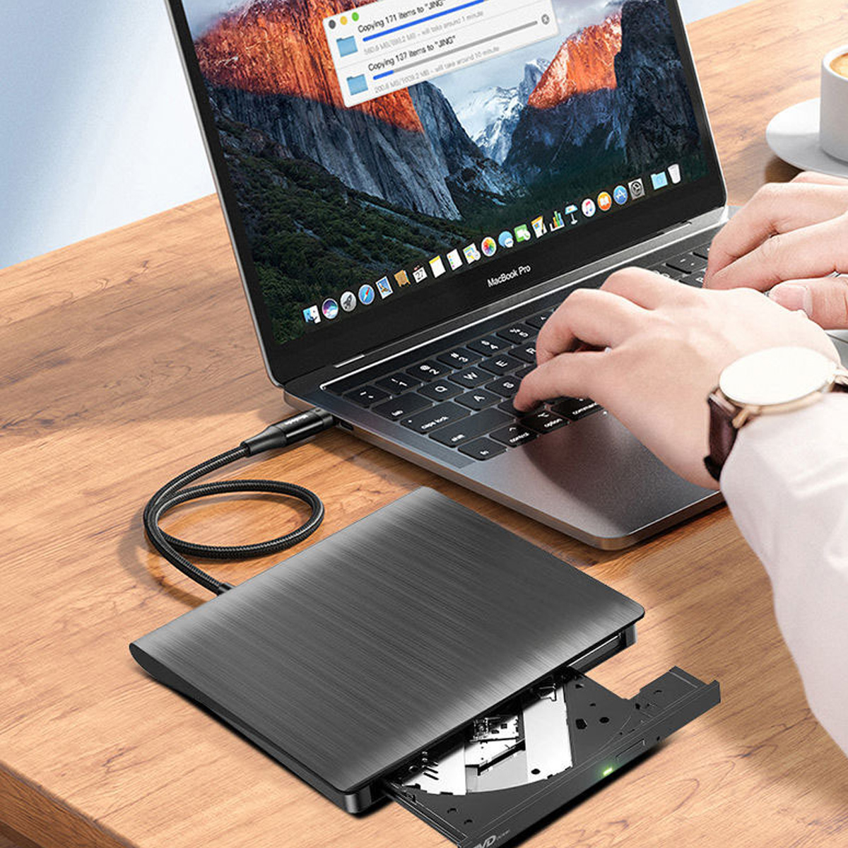 Ein externer CD/DVD-Brenner ist mit einem Laptop auf einem Holztisch verbunden, während jemand tippt.