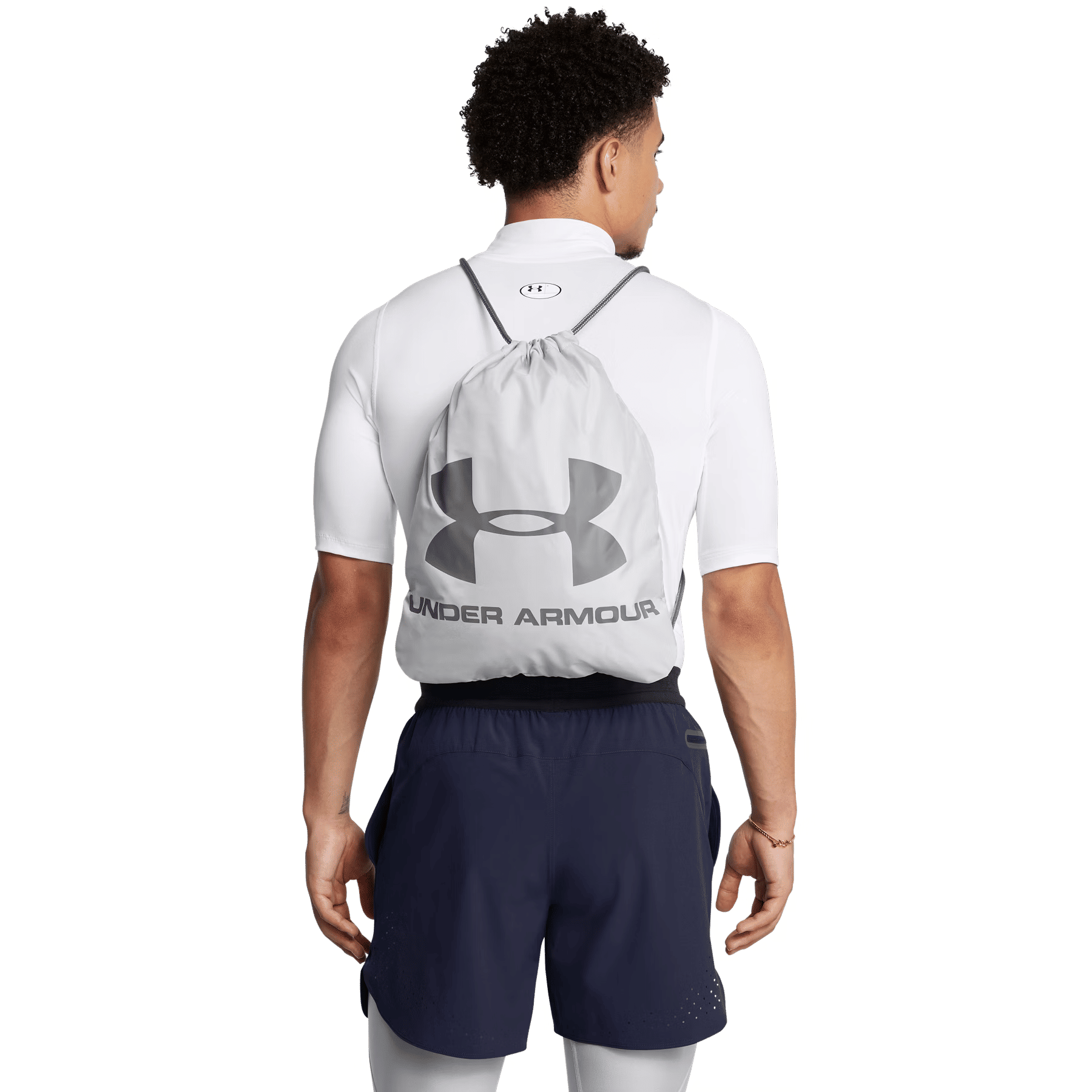 Rückansicht eines Mannes mit weißem Shirt, blauen Shorts und einem grauen Under Armour Turnbeutel vor schwarzem Hintergrund.