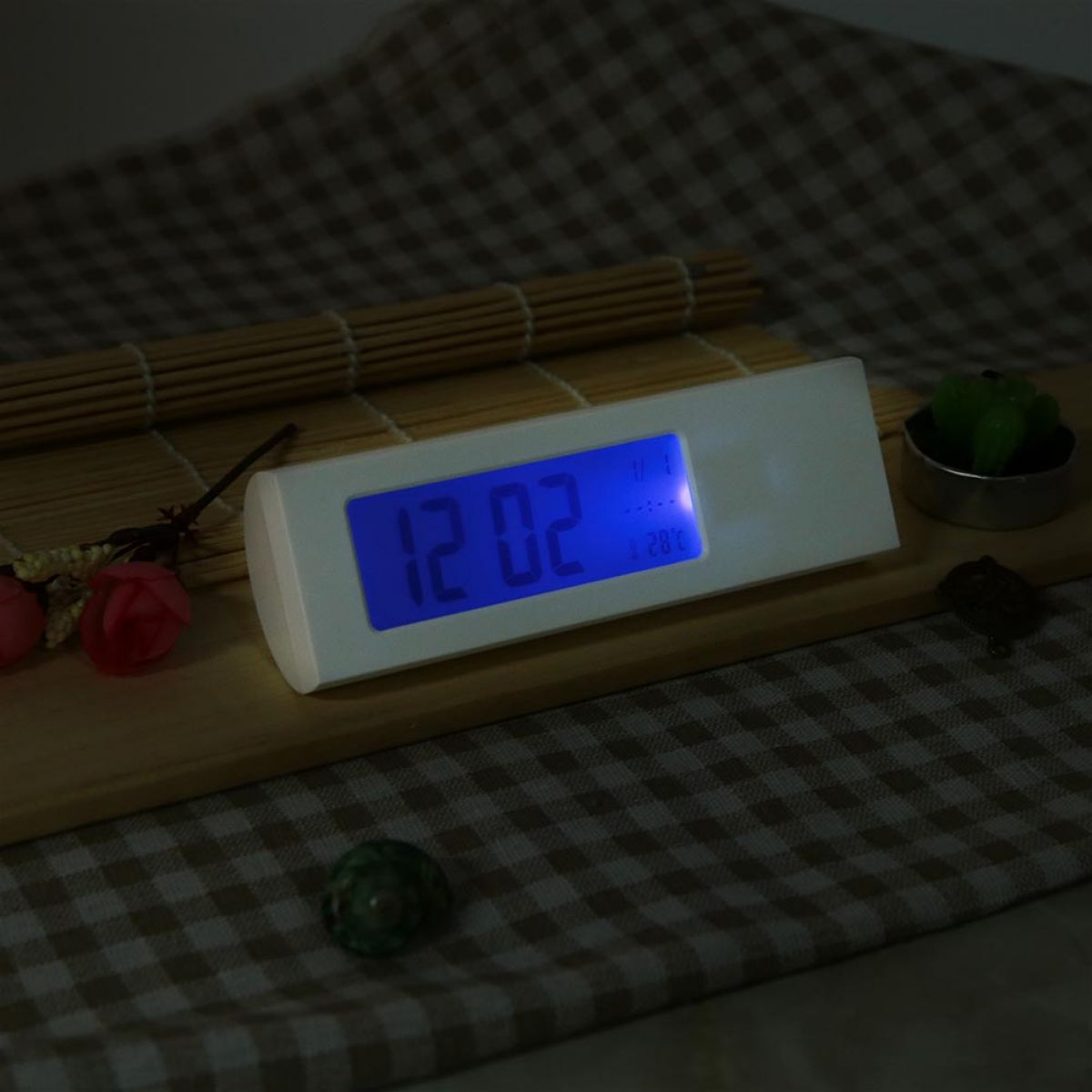 Eine weiße Digitaluhr mit blauem Display steht auf einem Holzbrett vor kariertem Hintergrund.