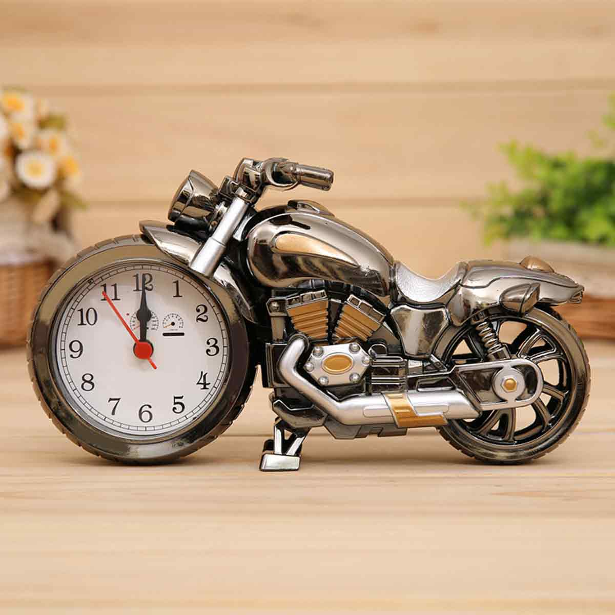 Eine metallische Motorrad-Tischuhr mit weißem Zifferblatt im Vorderrad auf hölzernem Untergrund.