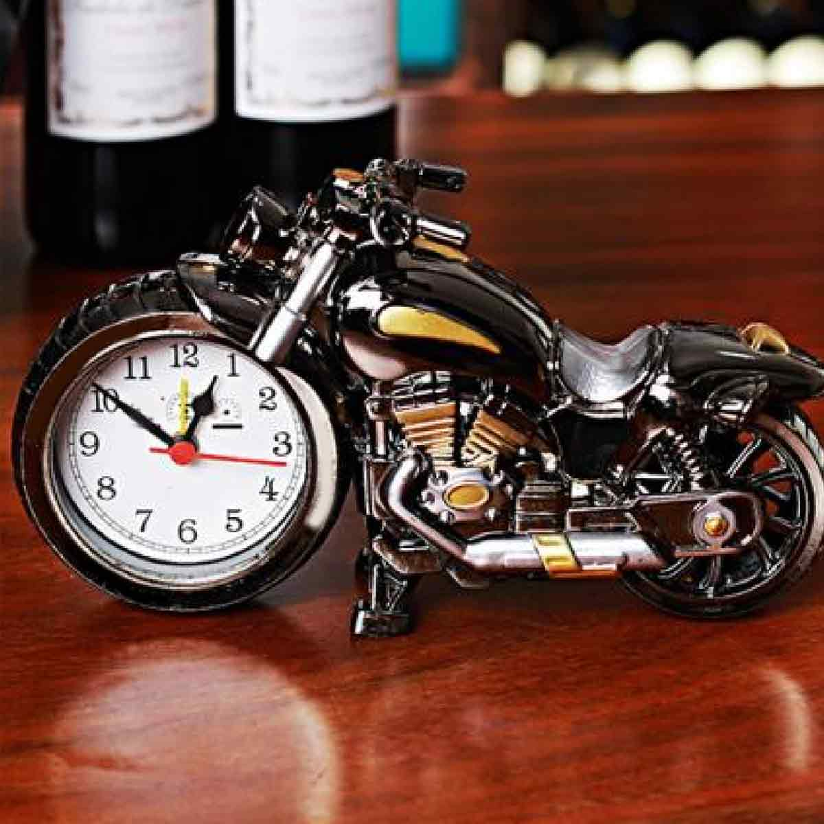 Eine schwarze Motorrad-Tischuhr mit weißem Zifferblatt steht auf einem Holzofentisch vor zwei Weinflaschen.