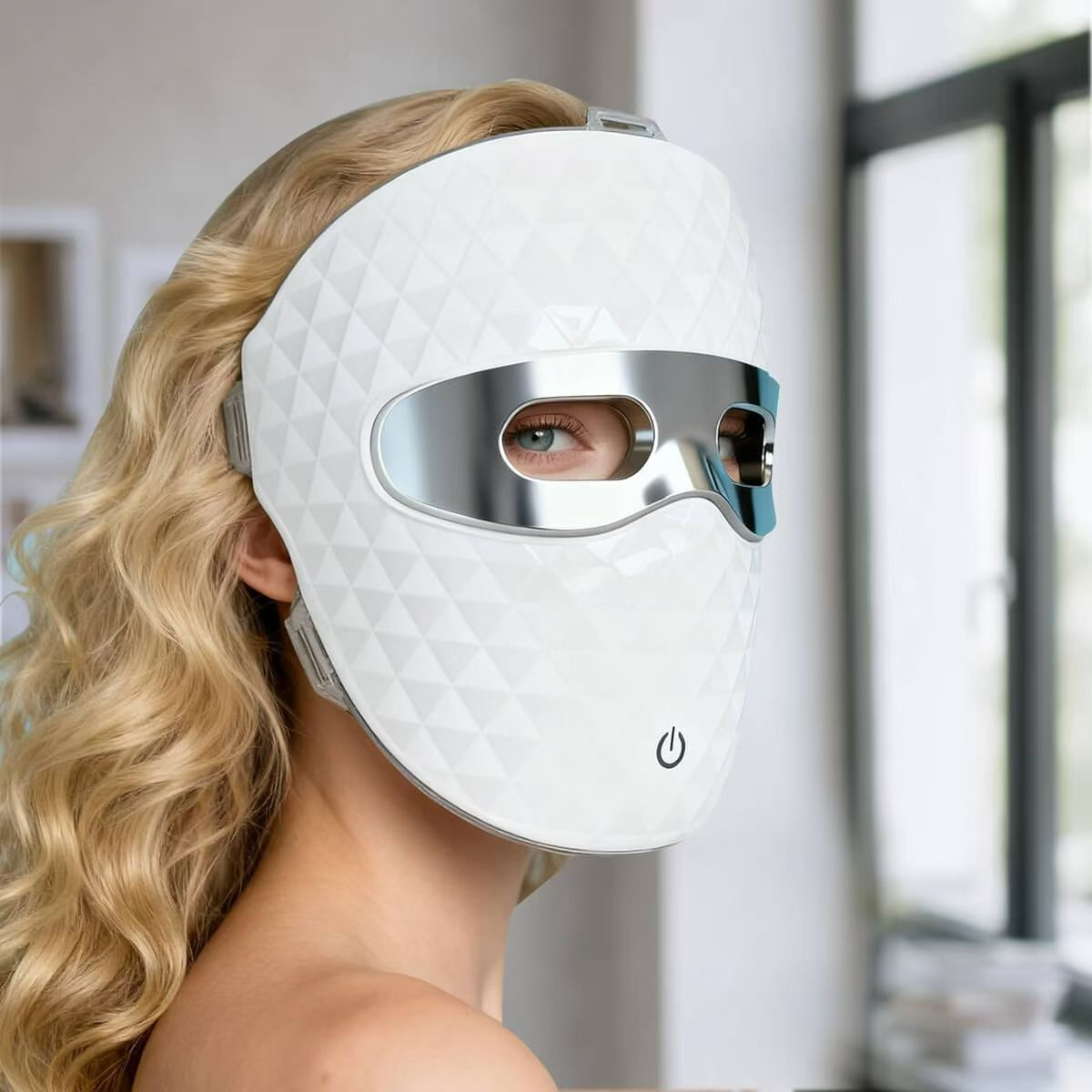 Eine Frau mit blonden Haaren trägt eine weiße LED-Gesichtsmaske mit silberner Augenpartie.