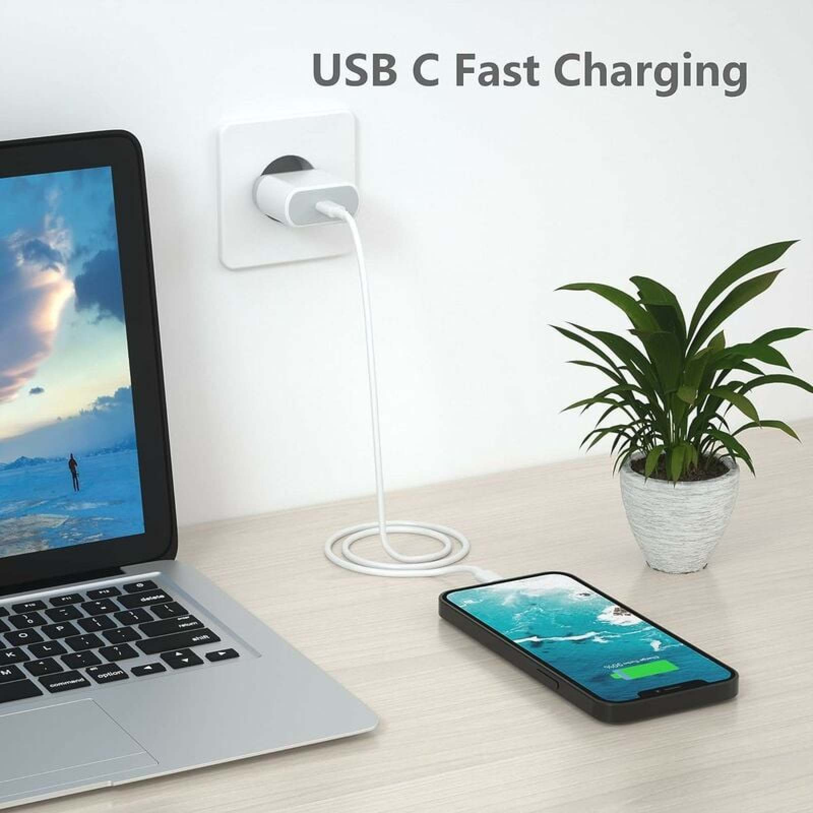 Ein Smartphone lädt über ein weißes USB-C-Kabel an der Wandsteckdose auf einem Schreibtisch mit Laptop und Pflanze.