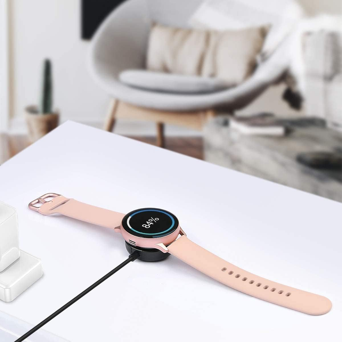 Eine rosa Smartwatch lädt auf einer weißen Oberfläche und zeigt 84 % Akku in einem hellen Raum.