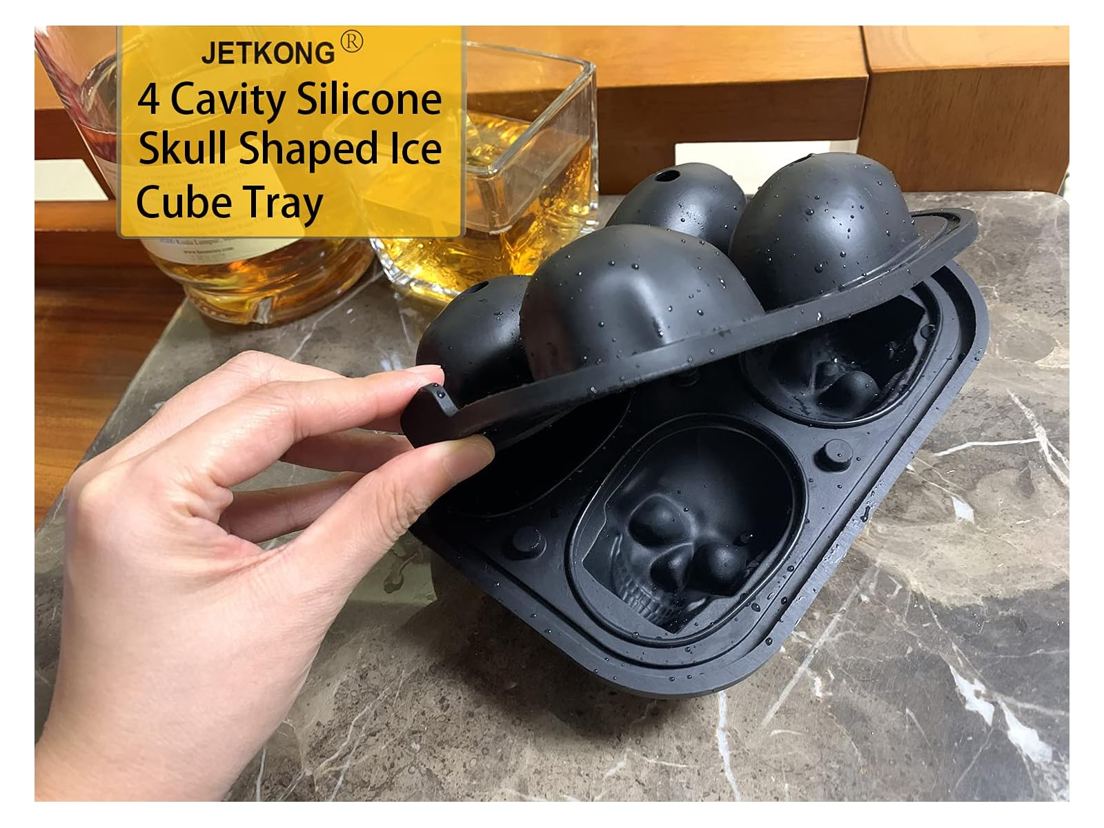 Eine Hand öffnet eine schwarze Silikon-Eiswürfelform mit vier Totenkopf-Förmchen auf einem Marmortisch.