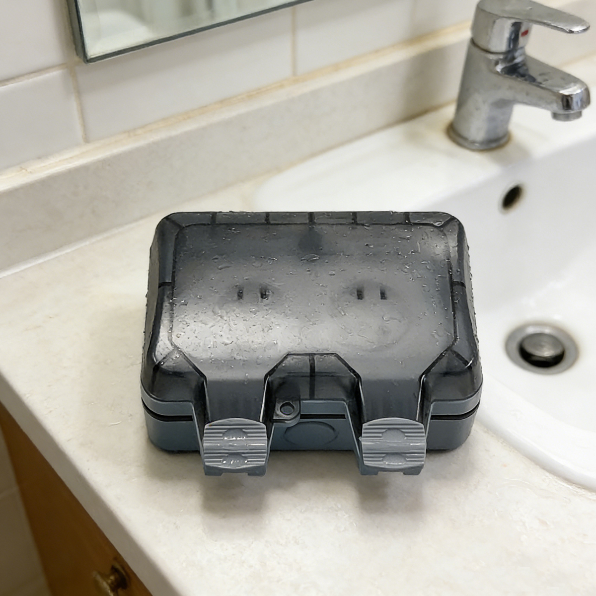 Eine nasse dunkelgraue Plastik-Wasserschutzabdeckung liegt auf dem Waschtisch in der Nähe eines Waschbeckens.