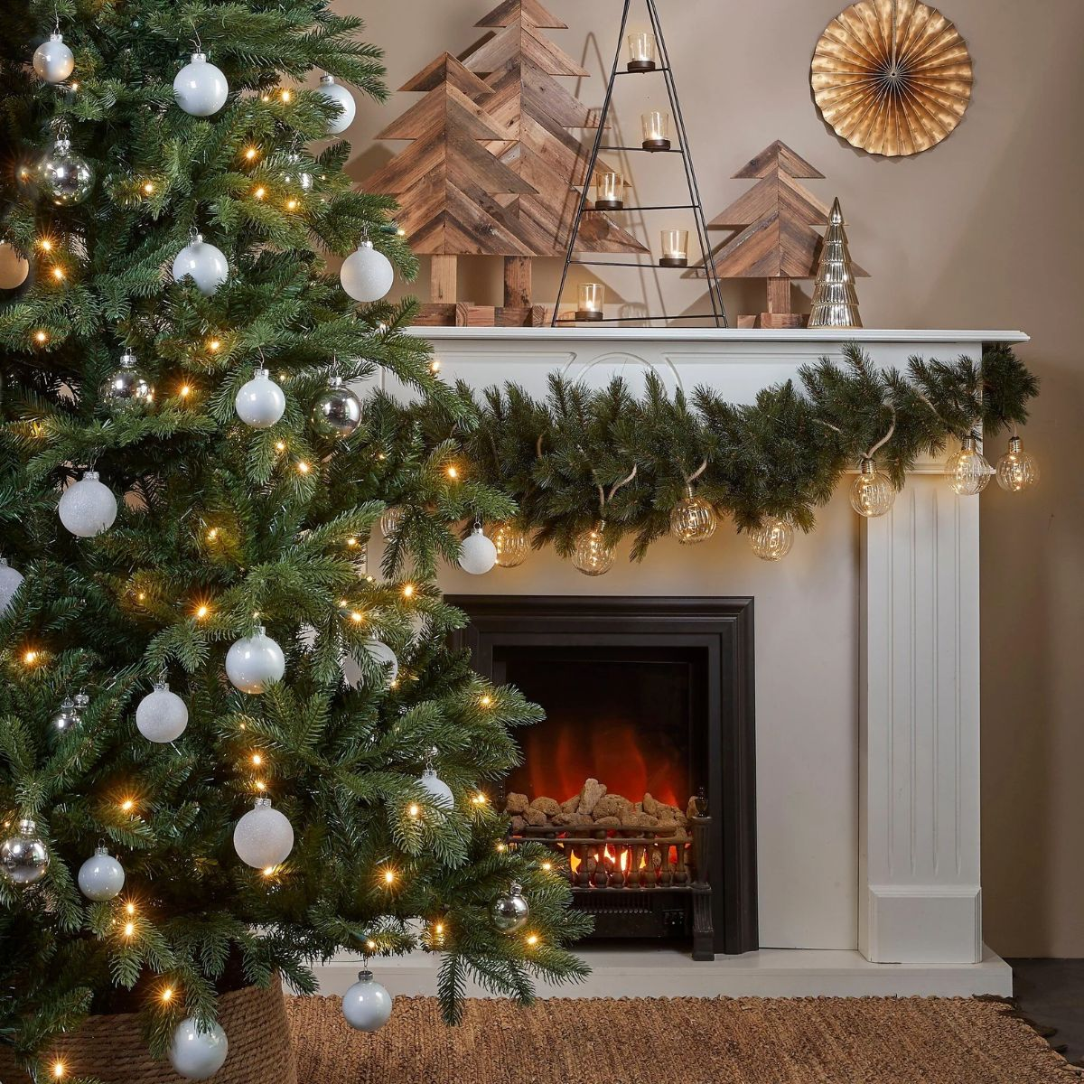 Kerstboom met witte kerstballen en lampjes voor een versierde haard.