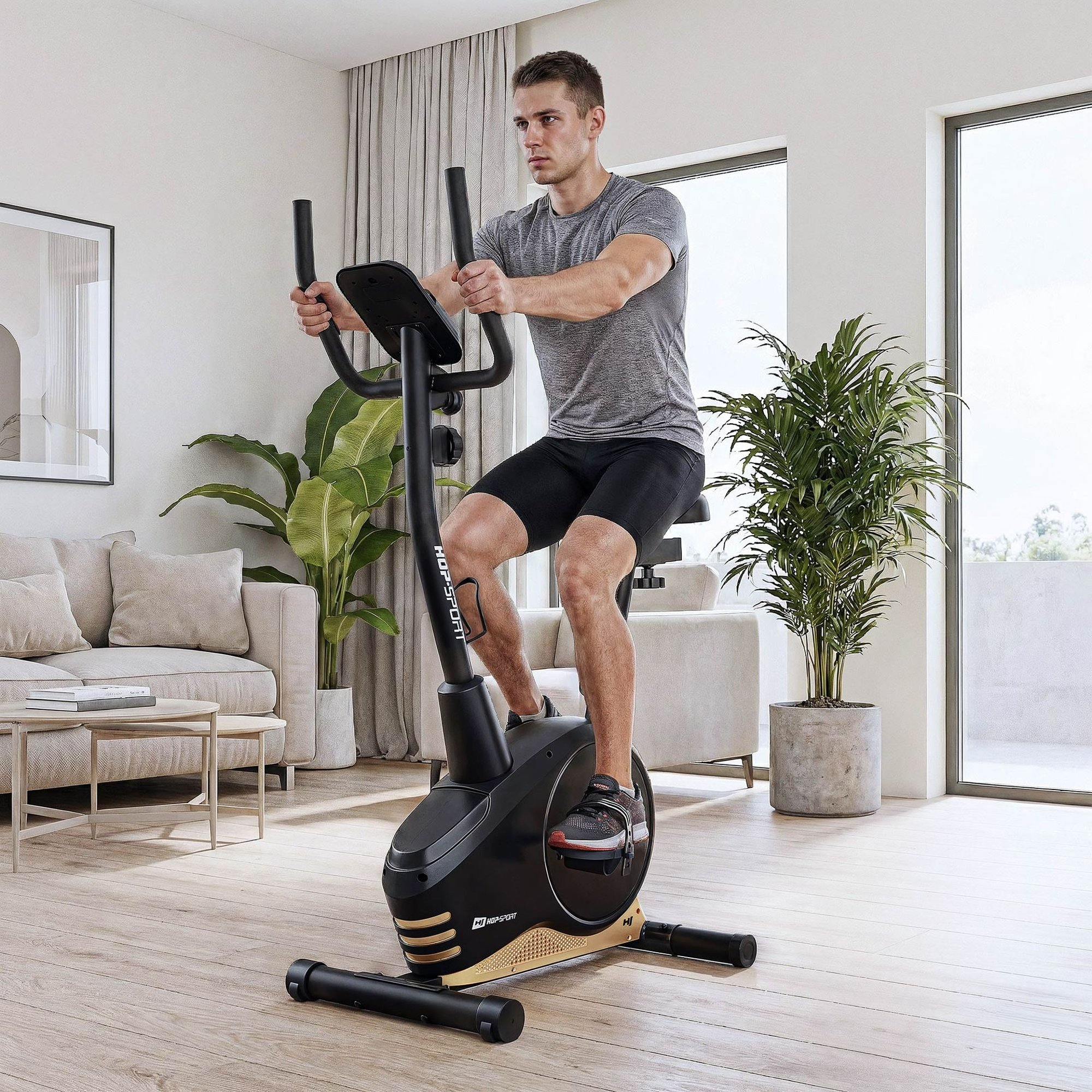 Ein Mann in grauem T-Shirt trainiert auf einem schwarzen Heimtrainer in einem hellen Wohnzimmer.