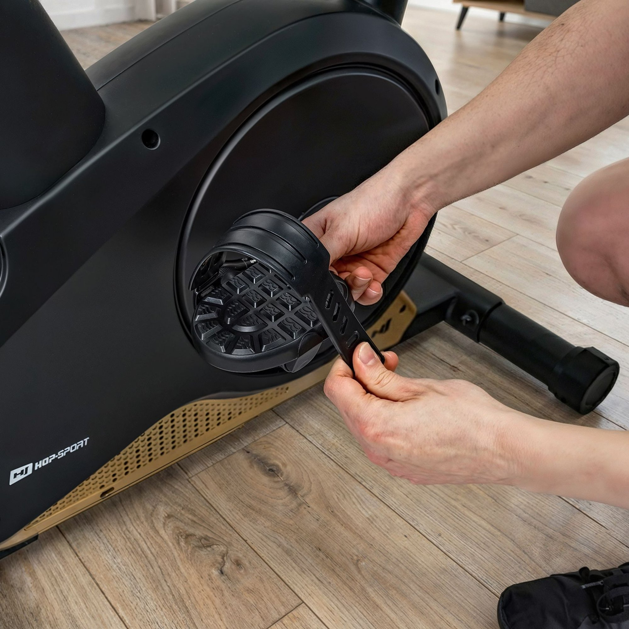 Eine Person befestigt einen Fußriemen an einem schwarzen Heimtrainerpedal.