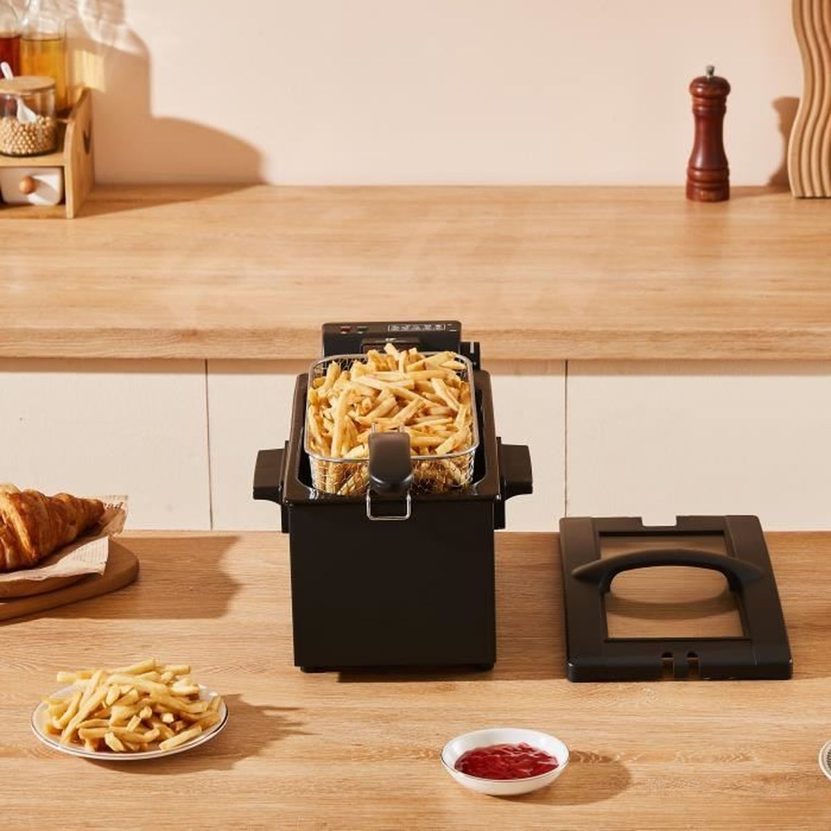 Una frgitrice nera piena di patatine fritte su un tavolo di legno, vicino a un piatto di patatine e ketchup.