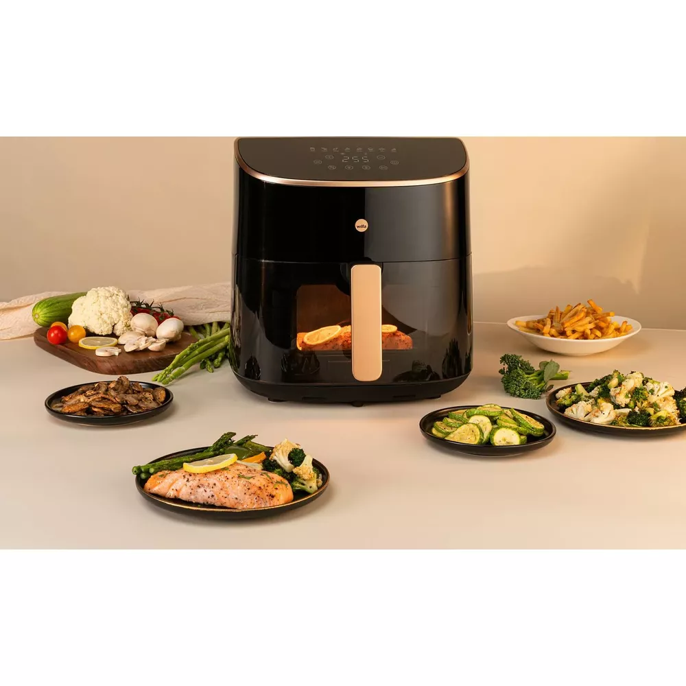 Schwarze Heißluftfritteuse umgeben von verschiedenen Tellern mit gesundem Essen wie Lachs, Gemüse und Pommes.