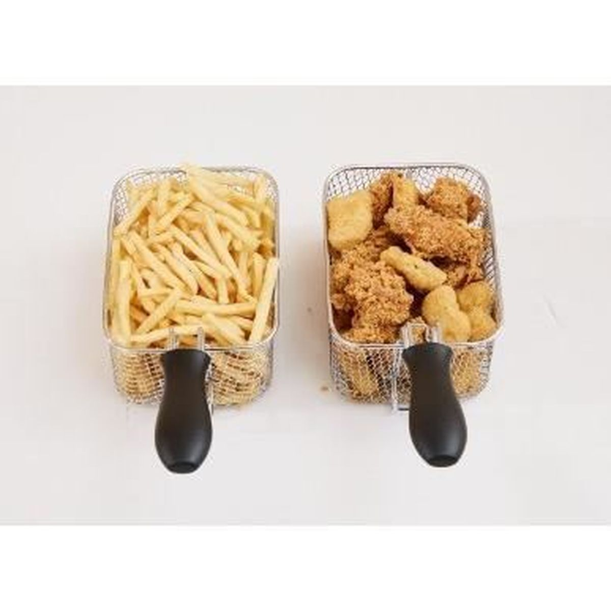 Due piccoli cestini di filo metallico con manici su un tavolo bianco, uno con patatine e l'altro con pollo.