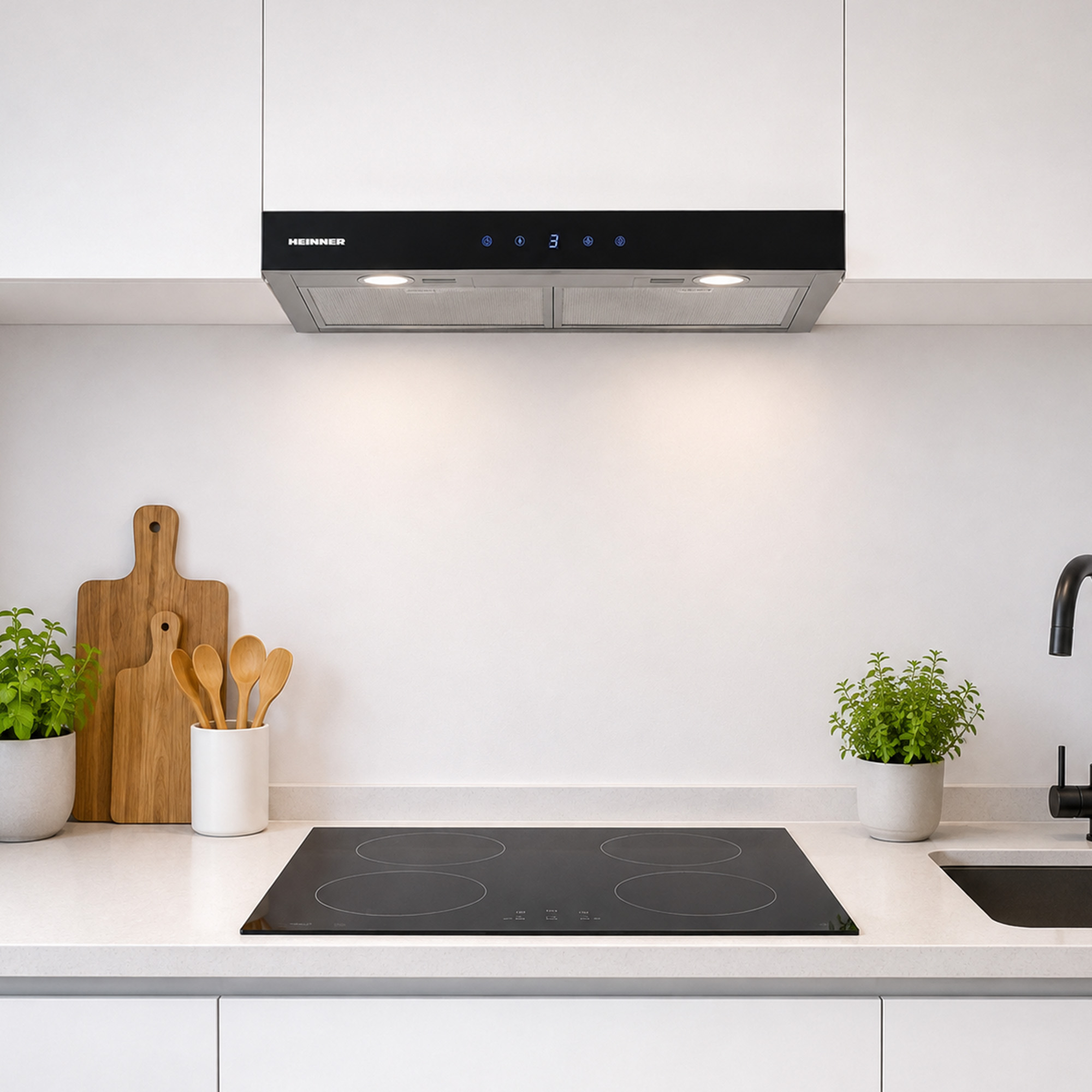 Modern kitchen with black induction hob, extractor hood, wooden spoons, and plants on a white countertop.