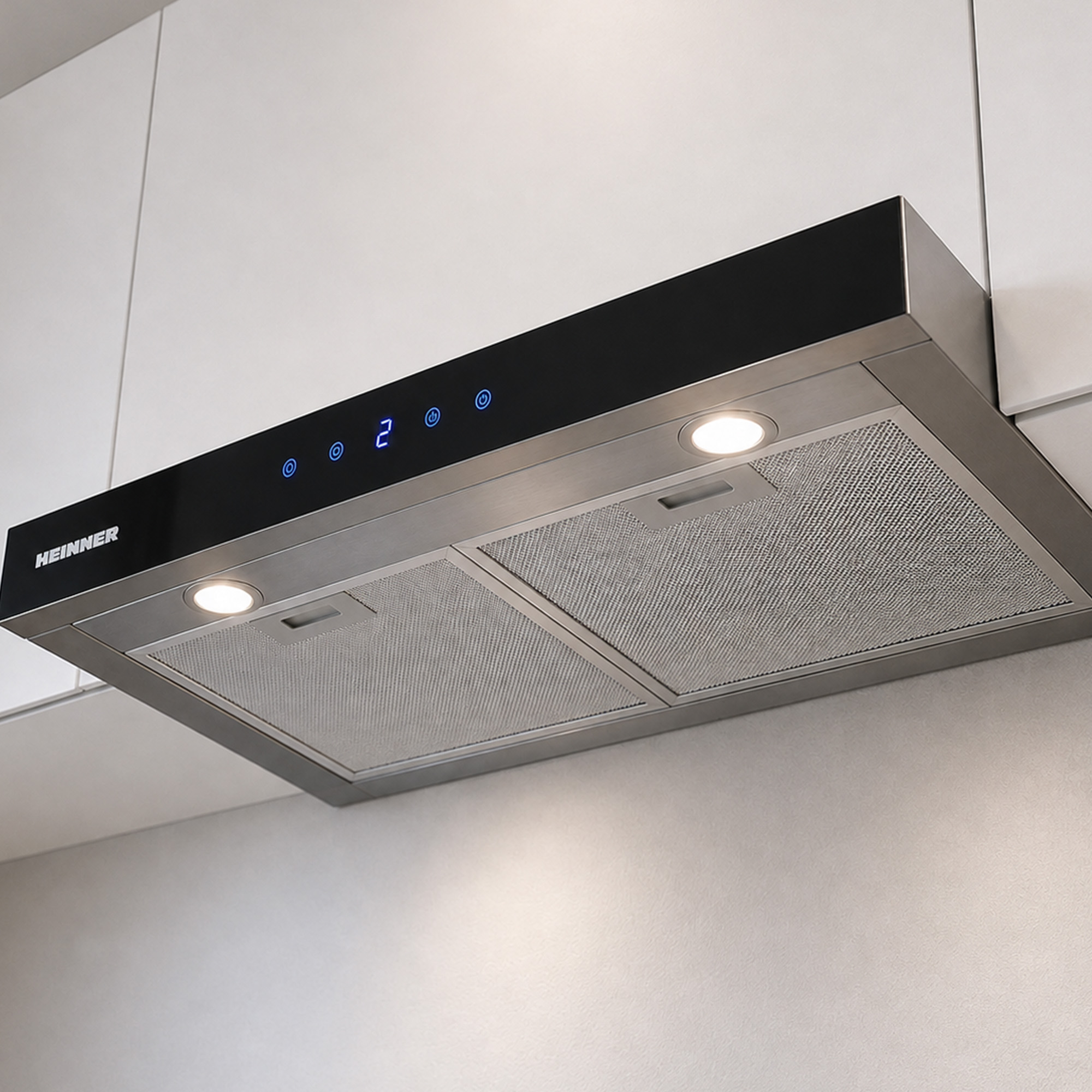 A stainless steel Heinner range hood with two mesh filters and integrated lights mounted under white cabinets.