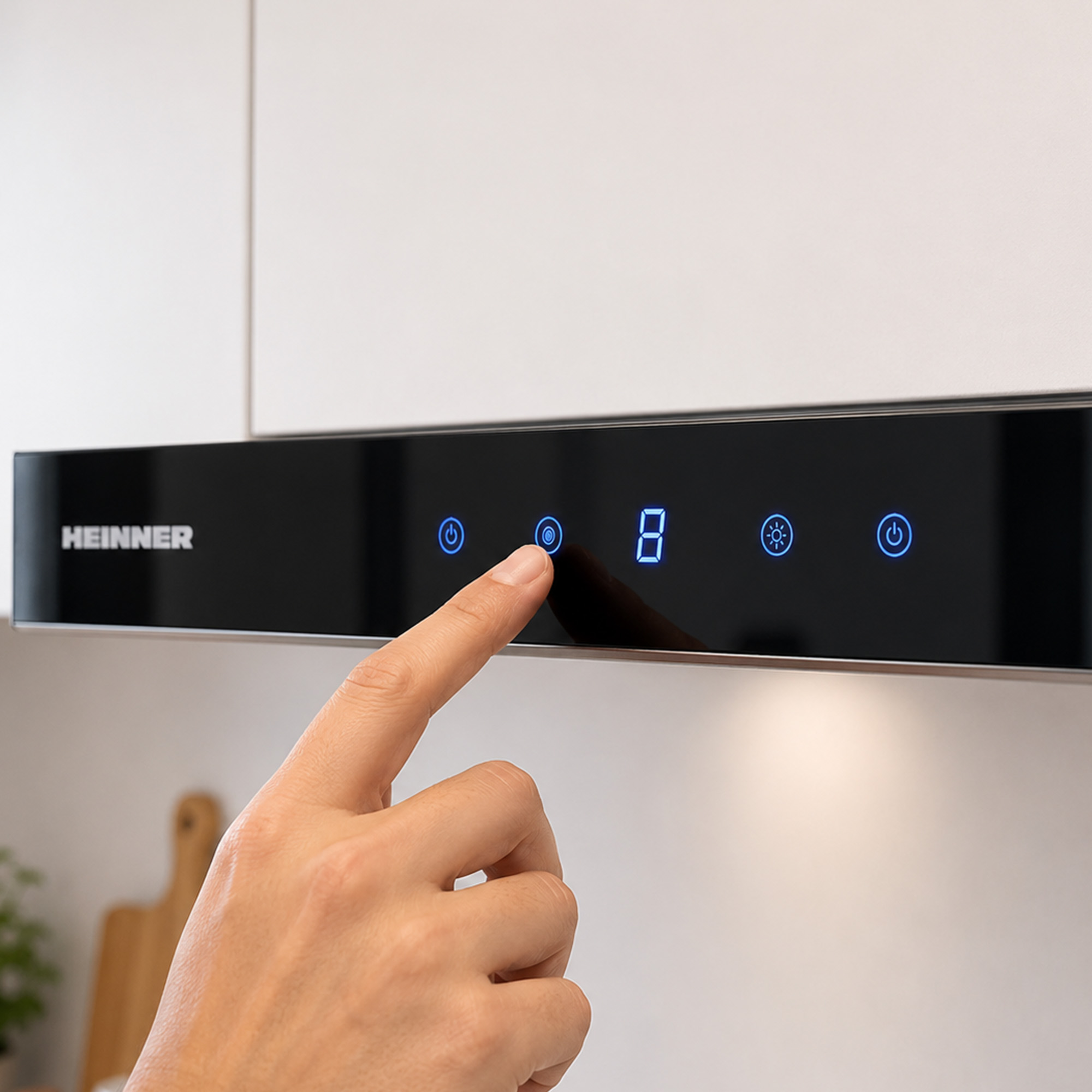 A hand operates the digital touch panel of a black cooker hood under white kitchen cabinets.