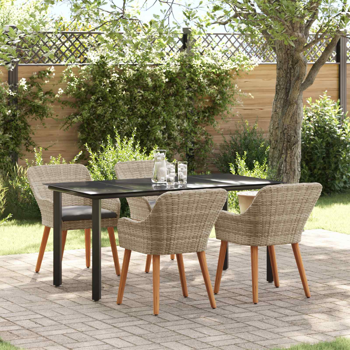 Una mesa de comedor negra con sillas tejidas en una terraza de piedra en un jardín, con una cerca de madera.