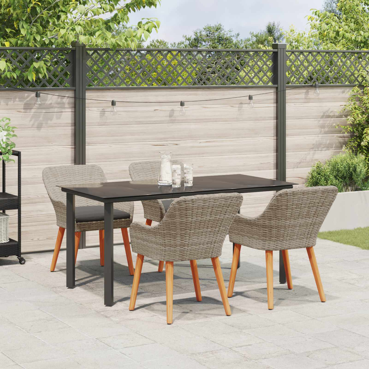 Mesa de comedor de mimbre y madera moderna con cuatro sillas en un patio de piedra frente a una cerca de madera.
