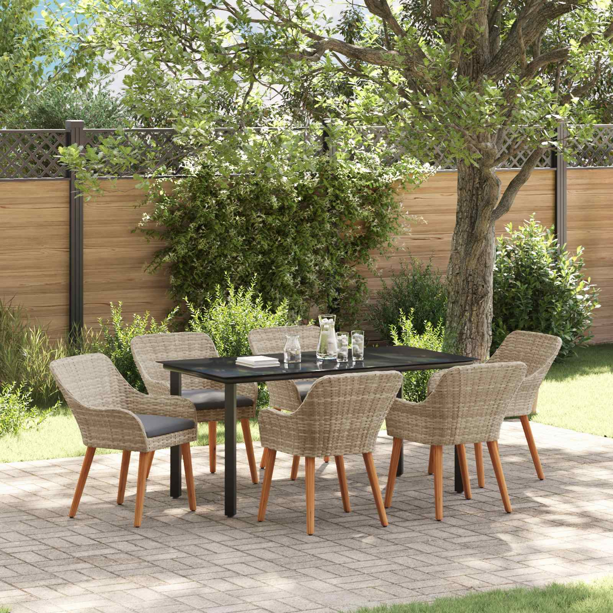Eine Essgruppe mit Tisch und Stühlen steht auf einer Steinterrasse im Garten unter einem großen Baum vor einem Holzzaun.