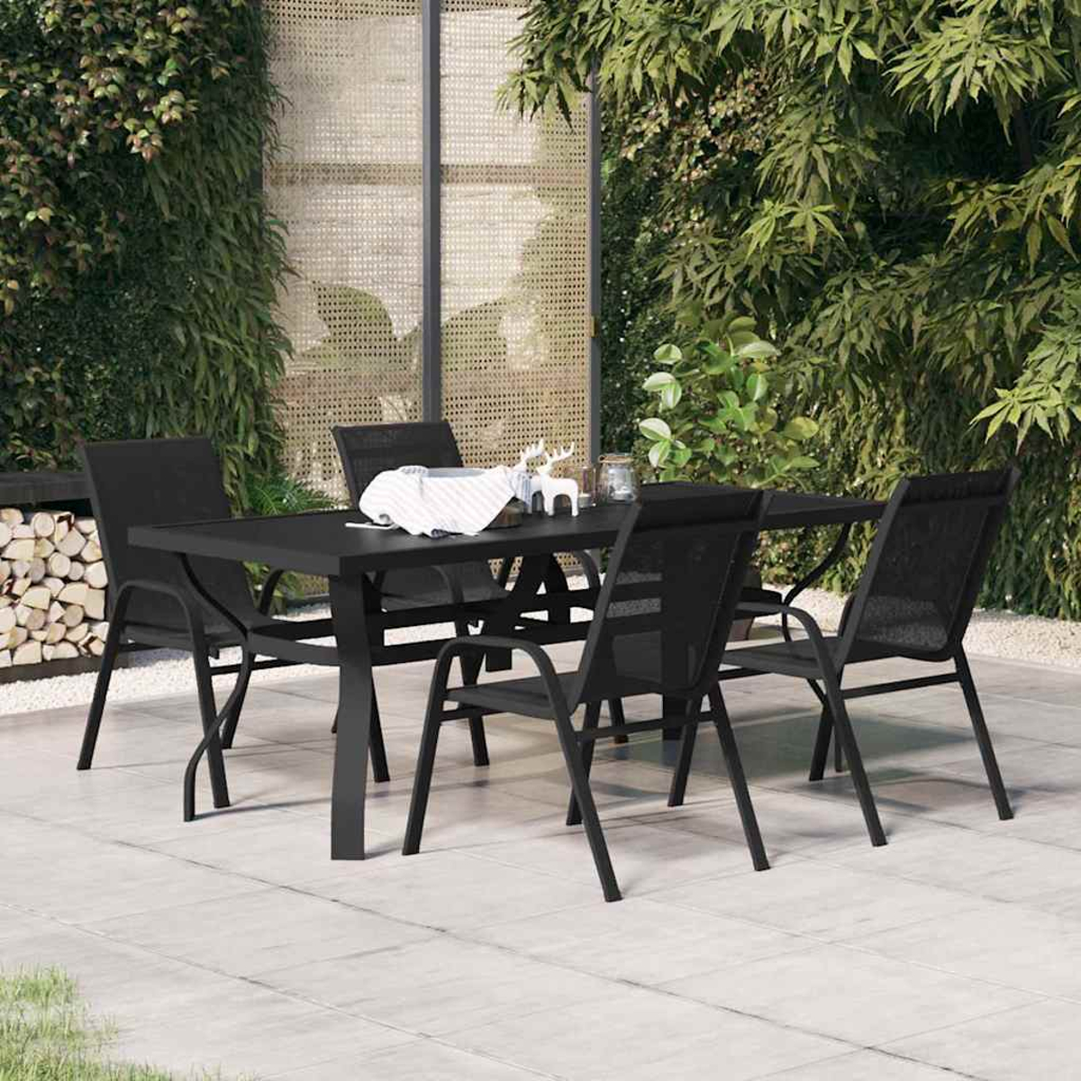 Ein schwarzer Gartentisch mit vier passenden Stühlen steht auf einer Terrasse vor einer grünen Hecke.