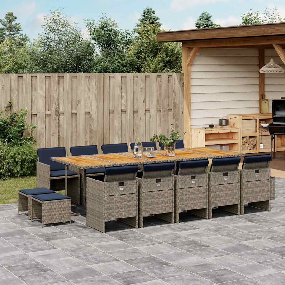 Ein großer Gartentisch mit Rattansesseln und Kissen steht auf einer Terrasse vor einer Holzwand.