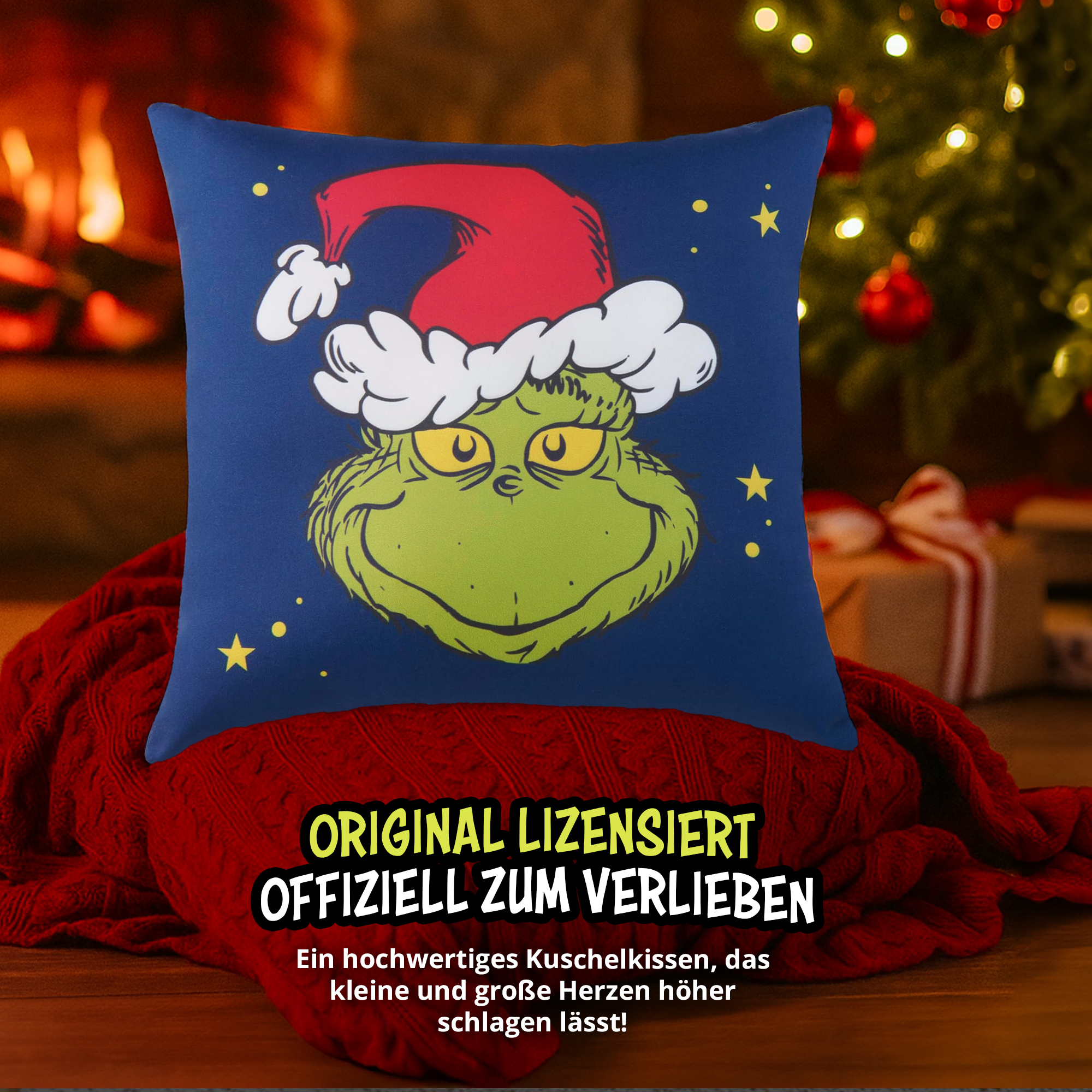 Ein blaues Kissen mit dem Grinch in Weihnachtsmütze liegt auf einer roten Decke vor Kamin und Tannenbaum.
