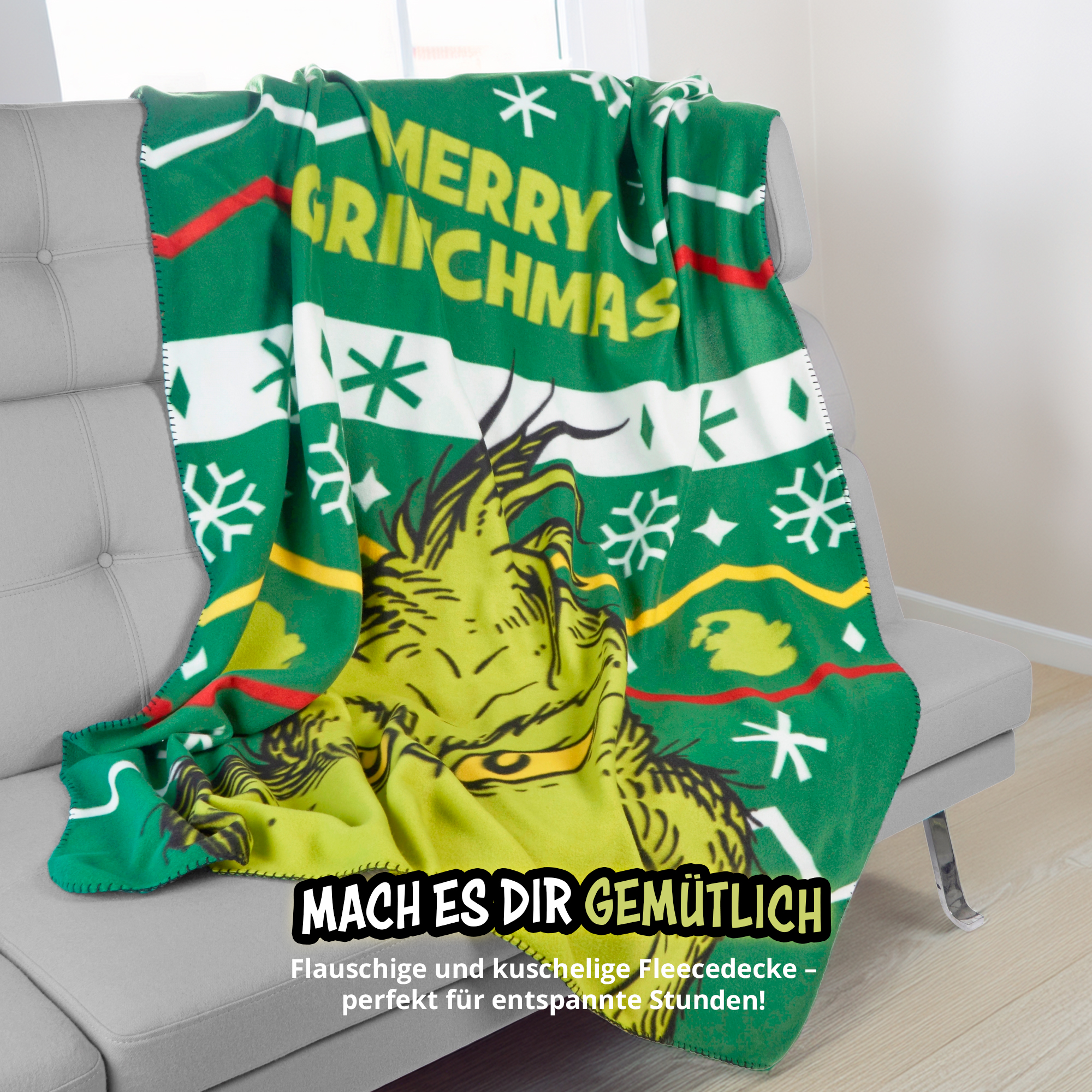 Grüne Grinch Fleecedecke mit Weihnachtsmotiven auf einem grauen Sofa.