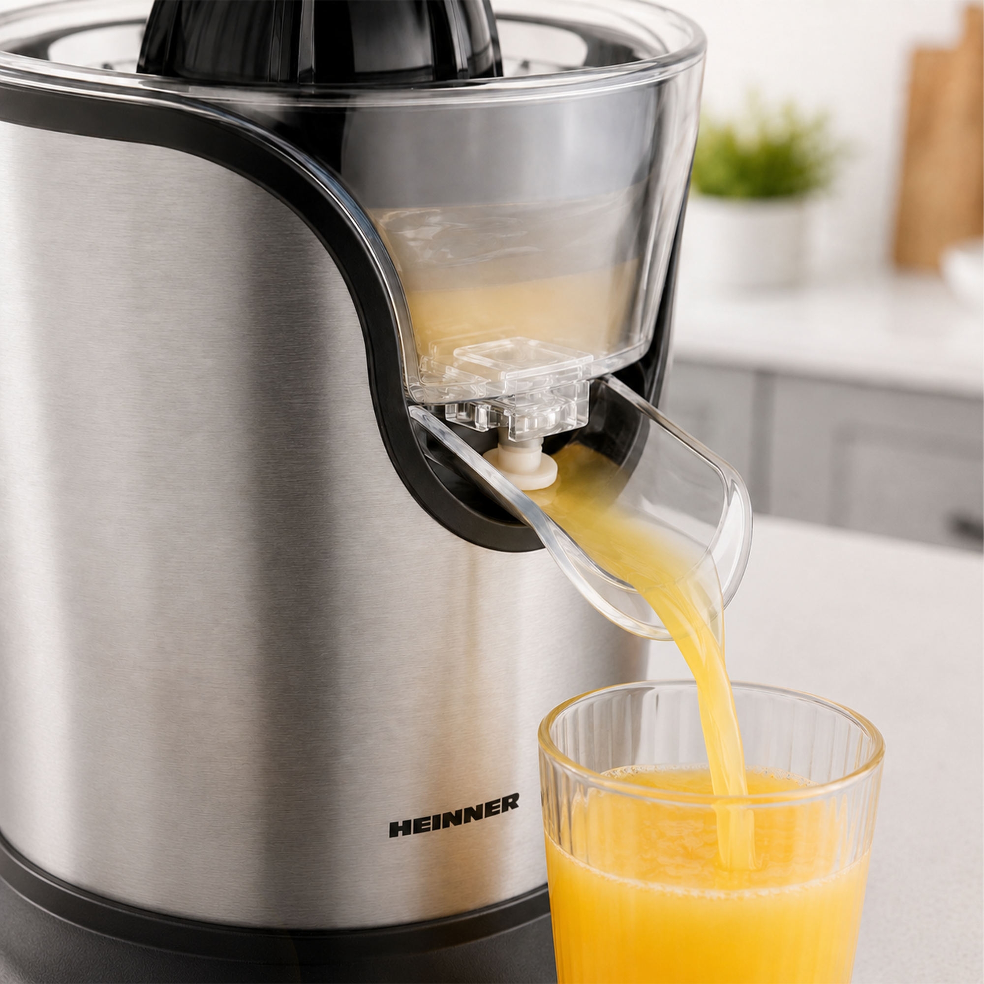 Frischer Orangensaft fließt aus einem silbernen Heinner-Entsafter in ein Glas auf einer Küchenarbeitsplatte.