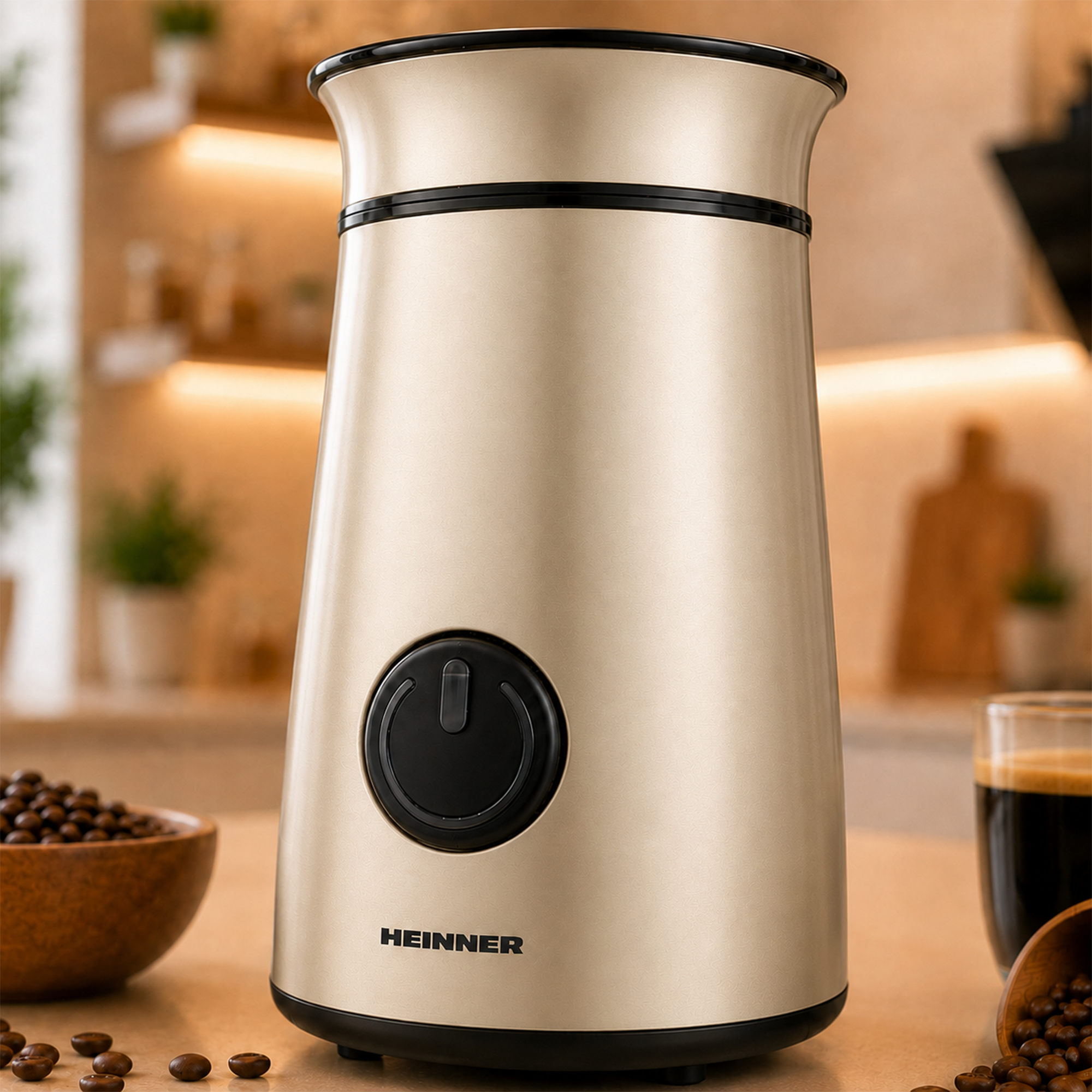 Eine champagnerfarbene Heinner Kaffeemühle auf einer Küchentheke mit Kaffeebohnen und einer Kaffeetasse.