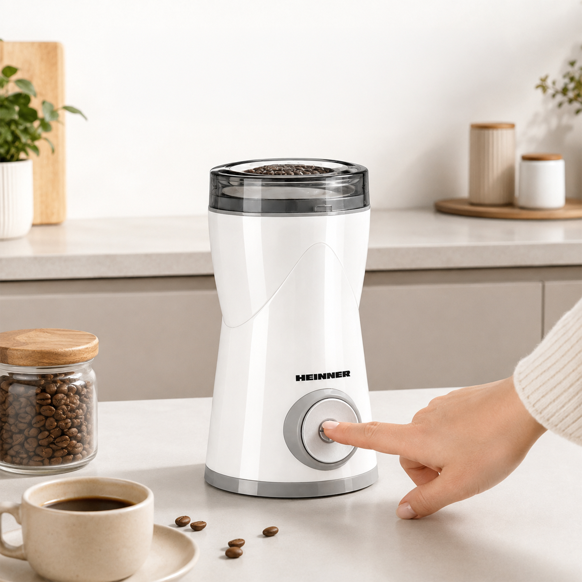 Une main appuie sur le bouton d'un moulin à café blanc sur un comptoir de cuisine avec des grains et une tasse.