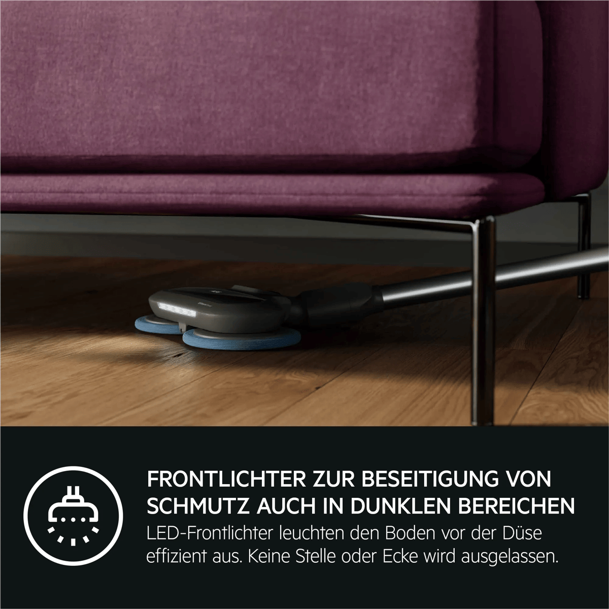Ein Staubsauger mit LED-Frontlichtern reinigt den Holzboden unter einem lila Sofa.